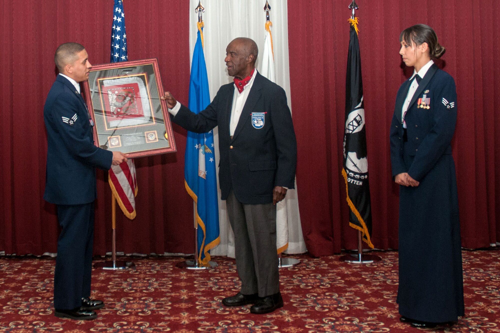 HANSCOM AIR FORCE BASE, Mass. – Senior Airman Matthew R. Ramos (left) and Senior Airman Ashley N. Lerke present retired Lt. Col. Enoch Woodhouse II the Bedford flag after he was the guest speaker at the Airman Leadership School Class graduation ceremony Nov. 22. Woodhouse is a native of Boston and an original member of the Tuskegee Airman. (Courtesy photo)