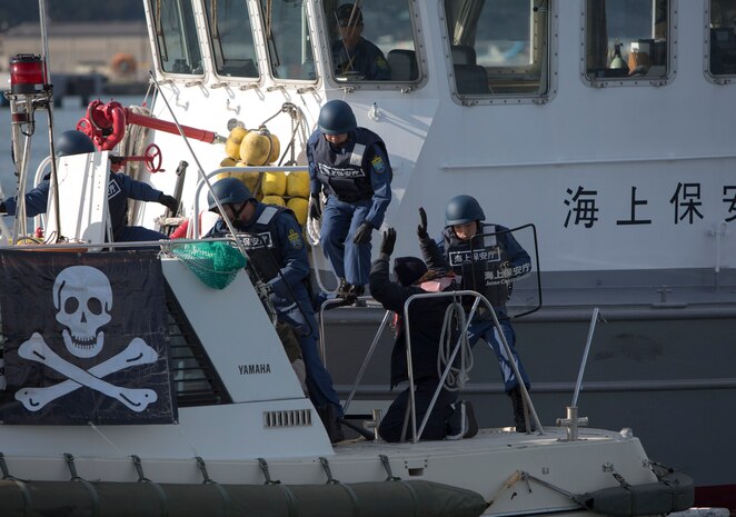 Iwakuni Coast Guard personnel board a cargo vessel during an anti-terrorism training exercise at Muronoki pier, Iwakuni harbor, Iwakuni, Japan, Nov. 22 2013. During a simulated patrol, Iwakuni Coast Guard engaged the enemy ship in a brief firefight with simulated rounds before disabling the vessel and apprehending the aggressors as part of their cooperative training with Iwakuni police and customs.