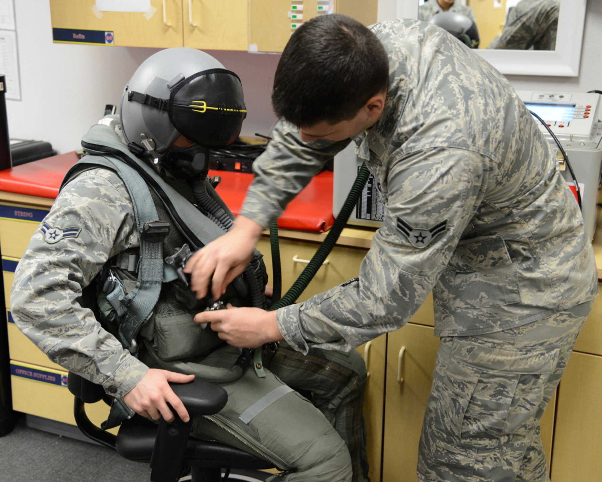 Airman 1st Class Jordan Theis, 3rd Operations Support Squadron, helps Airman 1st Class Grant Cook, 90th Aircraft Maintenance Unit, connect his aircrew flight equipment gear to an AFE tester at the 90th Fighter Squadron Nov. 15. (U.S. Air Force photo/Staff Sgt. Blake Mize)