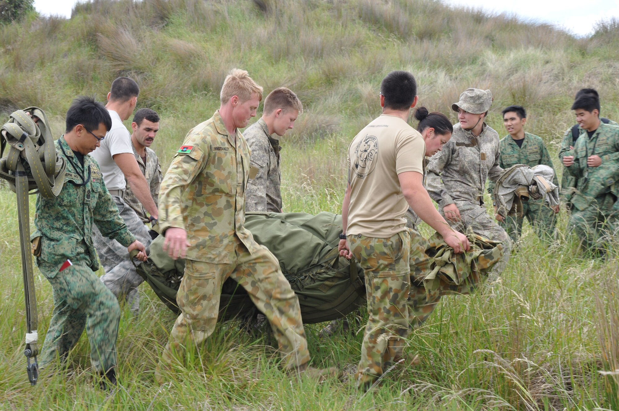 OHAKEA, New Zealand -- Uniformed service members representing four nations share the burden as they carry a recently-recovered main parachute to an awaiting transport vehicle during a combined cargo air-drop operation supporting Exercise Kiwi Flag at the New Zealand Defence Force Raumi Drop Zone near Ohakea, New Zealand. Kiwi Flag is a multilateral Royal New Zealand Air Force-sponsored tactical airlift exercise comprising air assets from the USAF, RNZAF, RAAF, RSAF and French Armed Forces of New Caledonia. (U.S. Air Force photo by Senior Master Sgt. Denise Johnson/Released)