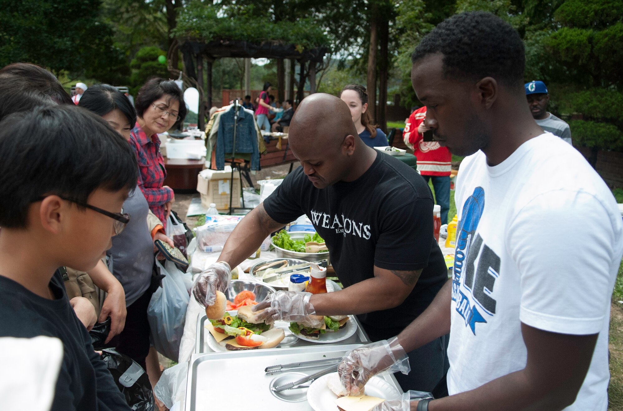 Technical Sgt. Terrance Tarleton, 8th Maintenance Group, middle, and Senior Airman Demeterius White, 8th Maintenance Group, right, serve hamburgers to guests during the Mount Saint Joseph Home for the Aged Family Day in Haewol-ri, Republic of Korea, Sept. 28, 2013. ( (U.S. Air Force photo by Tech. Sgt. Alex Griffin/Released)