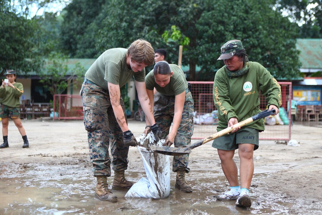 Liza N. Valencia, right, shovels mud into a sack held by Lance Cpl. Katherine B. Edelman, middle, and Lance Cpl. Emily E. Weber Sept. 29 as part of a community relations event at Olongapo City,  Zambales, Republic of the Philippines during Amphibious Landing Exercise 2014. During the event, Filipino police officers, community members and soldiers worked alongside U.S. Marines to clean three flood-affected schools. Training conducted during PHIBLEX 14 ensures Philippine and U.S. forces are capable of integrating effectively to conduct humanitarian assistance and regional security missions. The Filipino soldiers are with the Army Reserve Command. The Marines are with 3d Marine Expeditionary Brigade, III Marine Expeditionary Force. (U.S. Marine Corps photo by Lance Cpl. Jose D. Lujano/ Released)