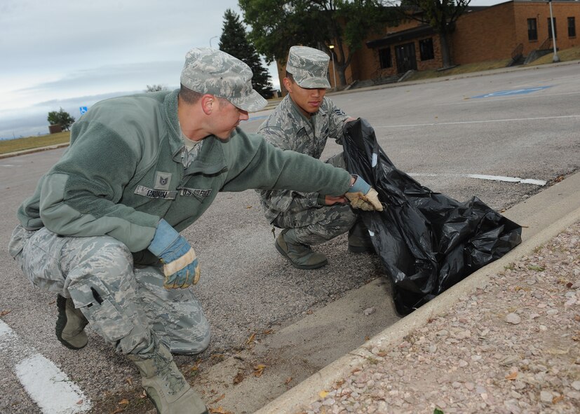 Tech. Sgt. Dallas Cronin, 28th Communication Squadron NCO in charge of client systems (left), and Senior Airman Luis Peralta, 28th CS resource advisor, remove leaves from a parking lot at Ellsworth Air Force Base, S.D. Sept. 27, 2013. Cronin and Peralta participated in a base-wide clean up, in an effort to improve the appearance of the base and keep the environment clean. (U.S. Air Force photo by Airman 1st Class Rebecca Imwalle/Released)