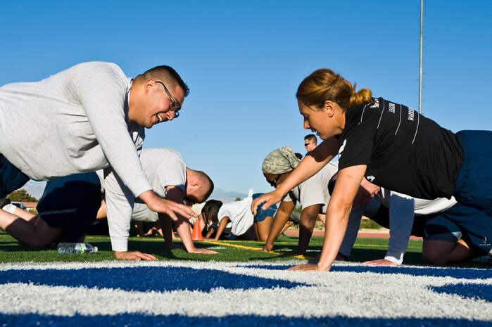 Tech. Sgt. Maria Miranda (right), 99th Security Forces flight chief, assists Staff Sgt. David Garcia (left), 99th SFS evaluator, during a warrior trained fitness workout on the field at the track behind the Warrior Fitness Center Sept. 26, 2013, at Nellis Air Force Base, Nev. The “Life of a Warrior” concept is a lifestyle incorporating good nutrition, healthy habits and a positive lifestyle. (U.S. Air Force photo by Airman 1st Class Christopher Tam)