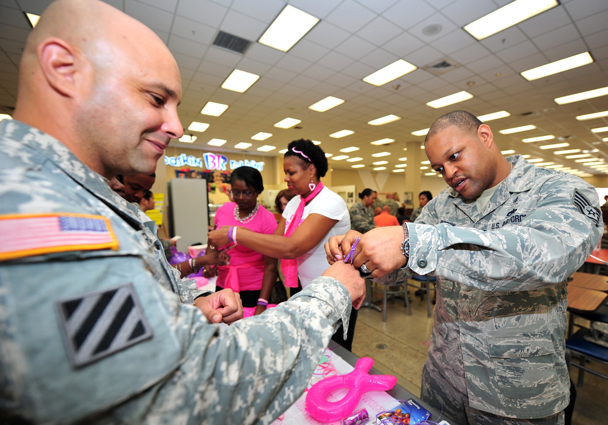 Staff Sgt. Kinsey Brown, right, 51st Medical Operations Squadron mental health technician, ties a symbolic ribbon on the finger of U.S. Army Chief Warrant Officer 2 Edwin Reyes, 3rd Battlefield Coordination Detachment airspace management chief, during a Breast Cancer and Domestic Violence Awareness Month display on Osan Air Base, Republic of Korea, Oct. 1, 2013. Visitors to the information table were encouraged to sign a pledge to support finding a cure for breast cancer and to report suspected domestic violence before having pink and purple ribbons tied to their fingers as reminders of their commitment. (U.S. Air Force photo/Airman 1st Class Ashley J. Thum)