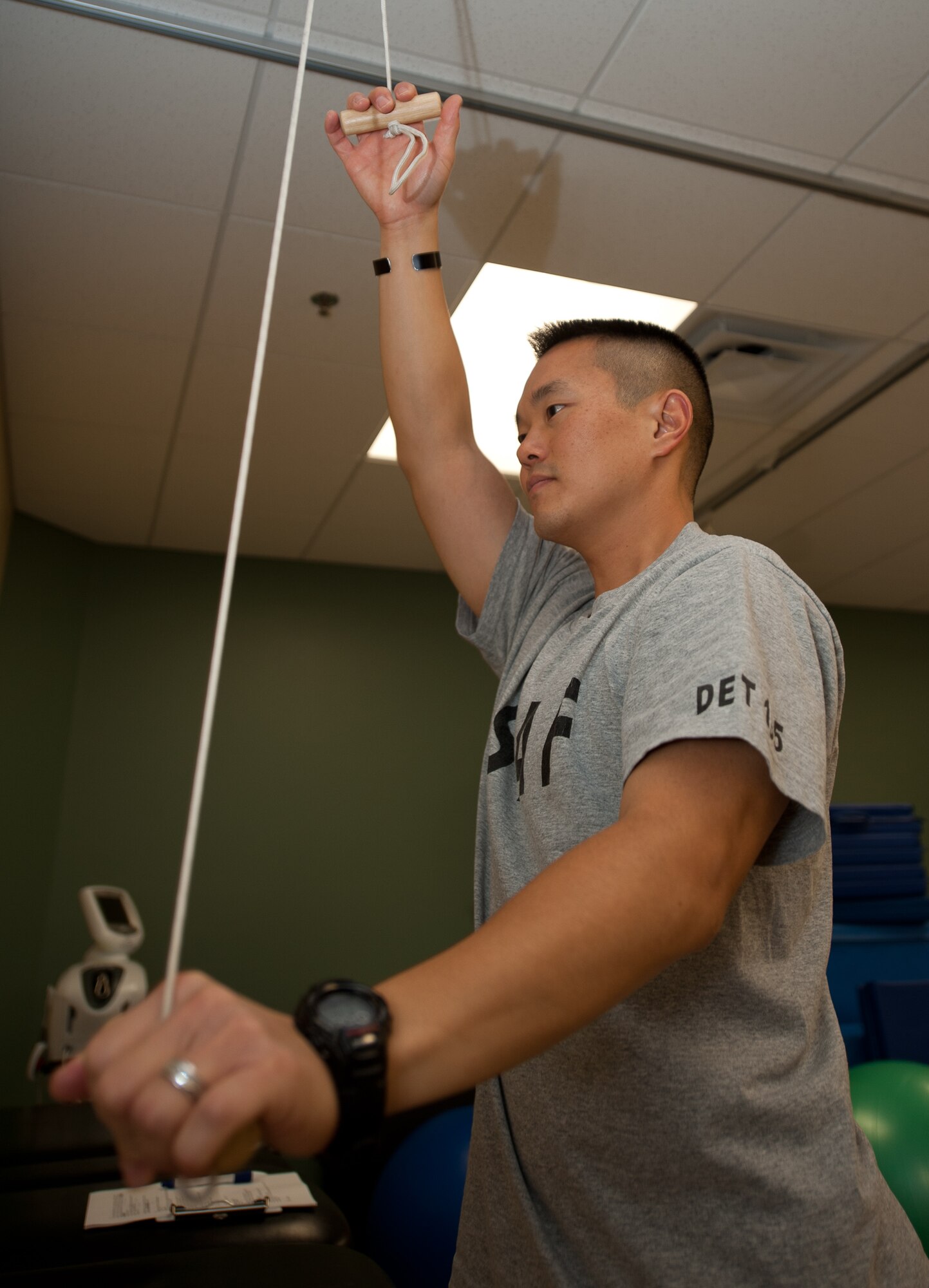 Capt. Chad Nishizuka, 34th Bomb Squadron chief of weapons and tactics, uses a pulley system to stretch during a physical therapy appointment at Ellsworth Air Force Base, S.D., Oct. 2, 2013. This system allows him to use his healthy arm to stretch his injured shoulder, resulting in a more effective stretch. (U.S. Air Force photo by Airman 1st Class Alystria Maurer/Released)