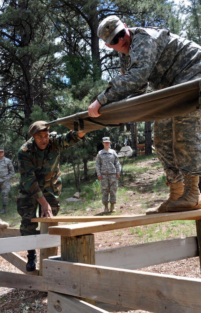 Suriname Army Maj. Richardo Breinburg hands Spc. Frank Doll, with the South Dakota Army National Guard, a stretcher while conducting a task on the Leader Reaction Course at West Camp Rapid, S.D., as part of the South Dakota Guard's Golden Coyote training exercise June 11, 2012. The South Dakota Guard hosted military leaders from the Republic of Suriname for a week long Subject Matter Expert Exchange.