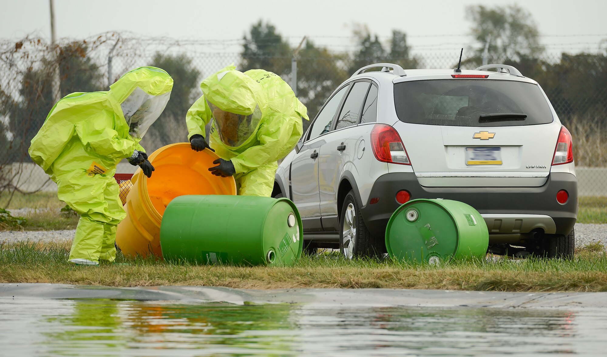 Staff Sgt. Jaimee Scott (left), 436th Aeromedical Squadron and Technical Sgt. Justin Alexander, 436th Civil Engineer Squadron wear bright green hazardous material protection suits as they approach a staged scene simulating a chemical spill with potential water contamination at Dover Air Force Base, Del. on Oct. 3, 2013. The airmen are participating in a joint unit training exercise between the 436th Medical Group and 436th Civil Engineer Squadron which tests the bases ability to respond to a natural disaster and resulting contamination to water supplies. This image has been altered to blur the license plate number from view of a personally owned vehicle. (U.S. Air Force photo/Greg L. Davis)