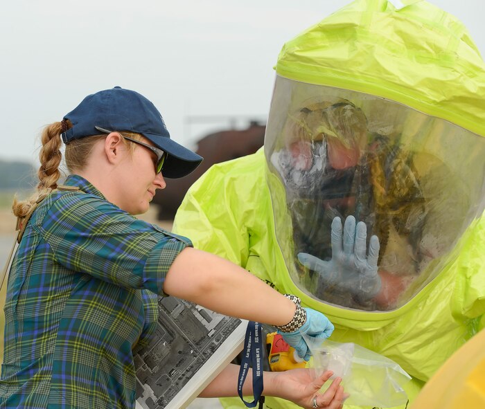 Jessica Feil of Alliance Solutions Group,( left) holds up an air-partical sensor so that Technical Sgt. Justin Alexander, 436th Civil Engineer Squadron can read the screen during a simulated contamination exercise at Dover Air Force Base, Del. on Oct. 3, 2013. Alexander uses his hand to wipe away fog on the inside of his hazardous material suit. The exercise tested the bases ability to respond to a natural disaster and resulting contamination to water supplies. (U.S. Air Force photo/Greg L. Davis)