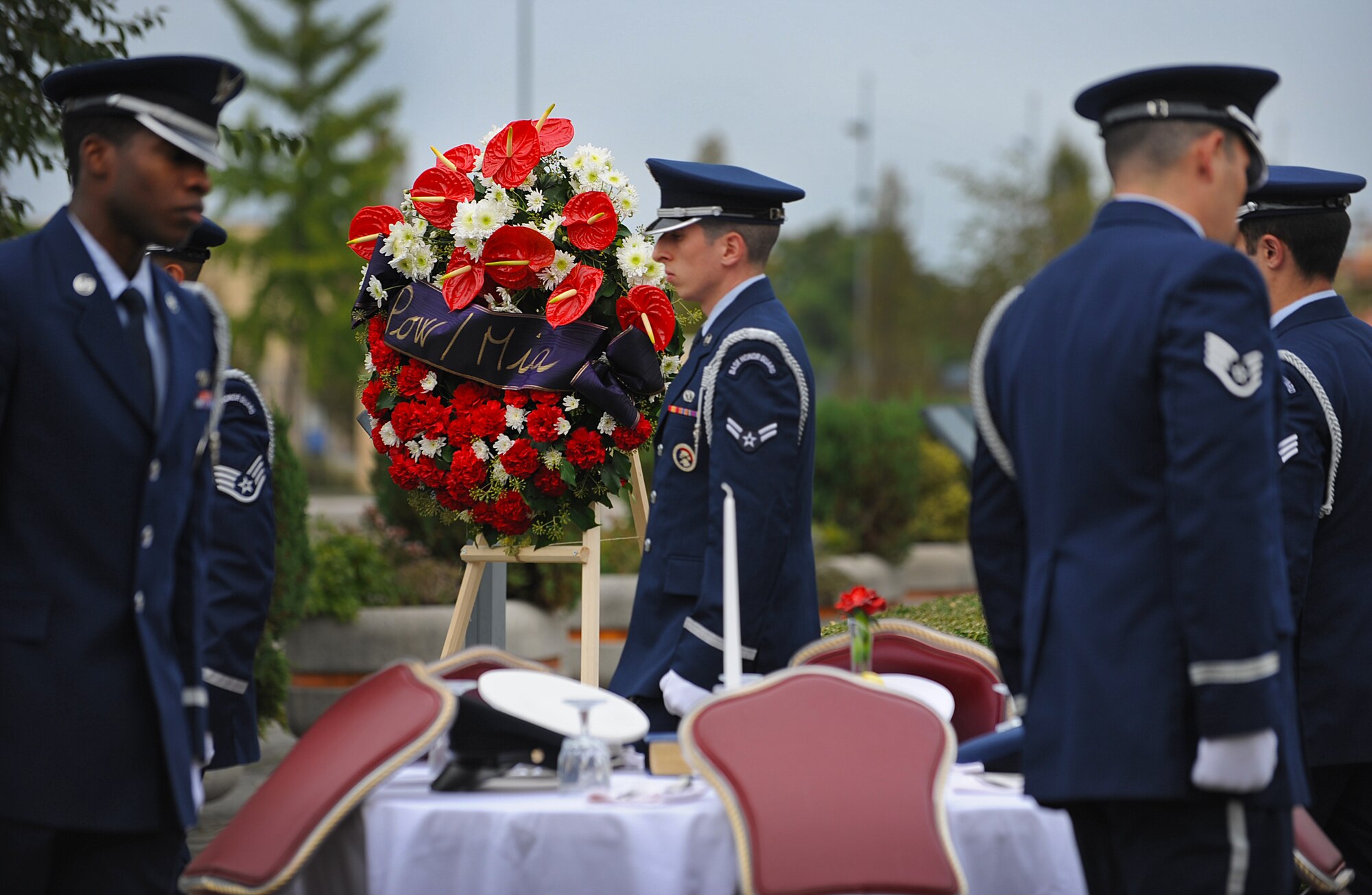 Members from the honor guard place the five services’ caps on a table to represent the Prisoners of war/Missing in action during a ceremony, Oct. 3, 2013, at Aviano Air Base, Italy. A slice of lemon on a bread plate is to remind us the bitter fate of those captured and missing in a foreign land. A pinch of salt symbolizes the tears of those missing and their families who seek answers. A table and chair are used as a symbol for the missing, thus reserving a chair in hopes of their return. (U.S. Air Force photo/Airman 1st Class Matthew Lotz)
