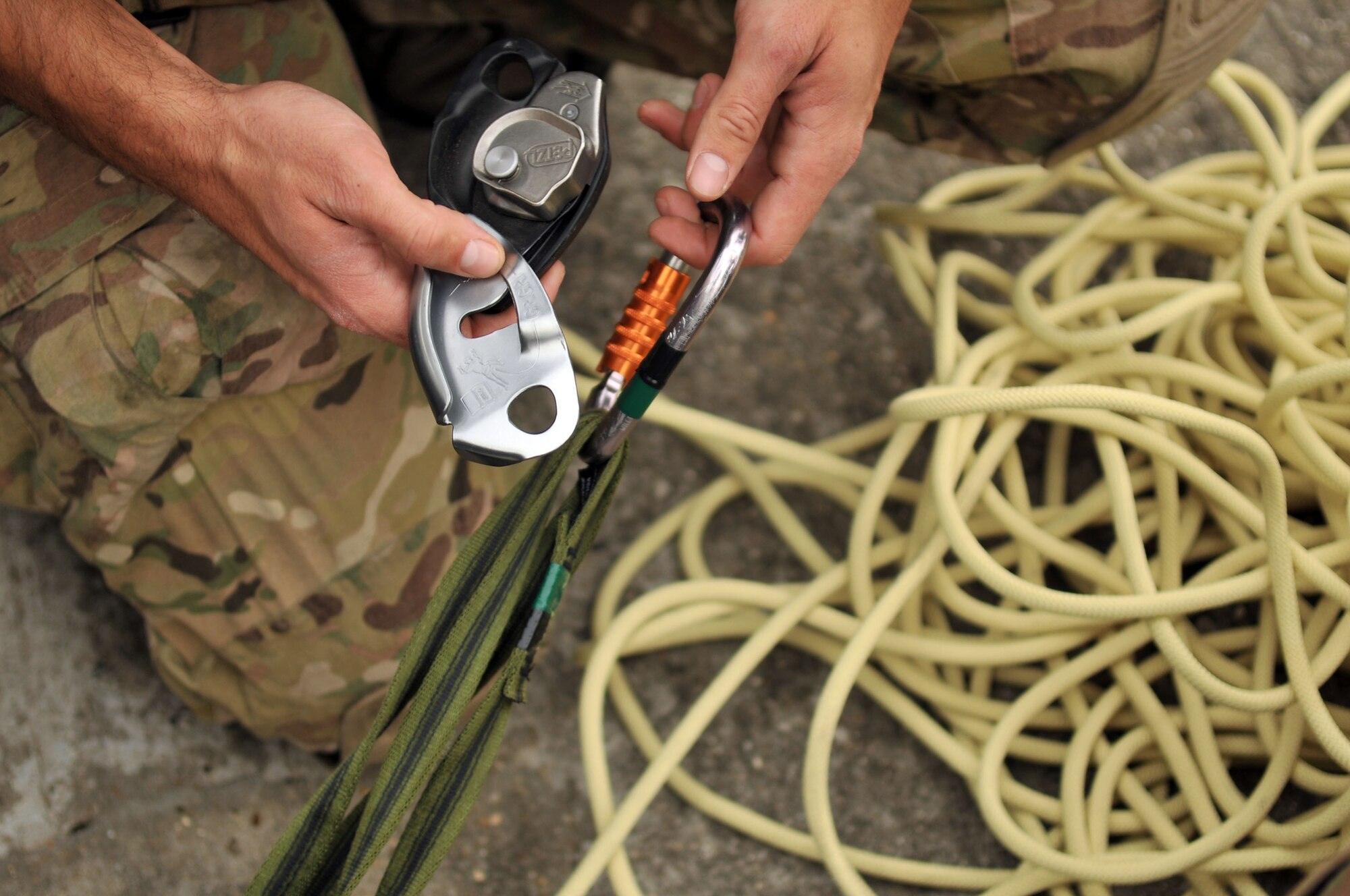 U.S. Air Force Staff Sgt. Trevor Clark, 321st Special Tactics Squadron pararescueman, attaches a carabineer to a belaying device as he hooks up the tubular nylon of the extraction gurney Oct. 2, 2013, on RAF Mildenhall, England. Clark assisted in the recovery of simulated wounded personnel during the confined-space extraction exercise. Pararescuemen are the most highly-trained and versatile Personnel Recovery specialists in the world, and will do whatever is required to deny the enemy a victory and bring our warriors home to fight another day. (U.S. Air Force photo by Airman 1st Class Kyla Gifford/Released)