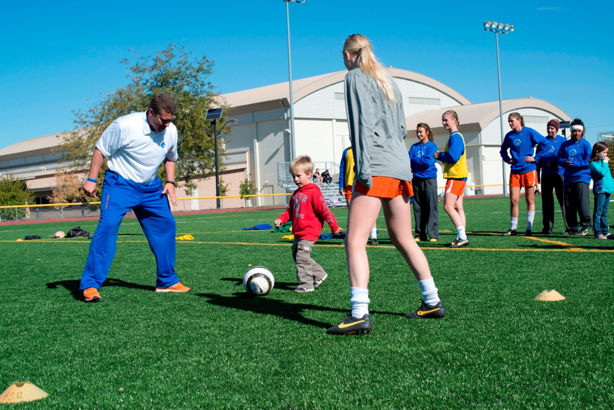 Three-year-old Elijah Carlsness, son of Tech. Sgt. Tim Carlsness, 366th Operations Support Squadron, dribbles a ball between a Boise State University ladies soccer player and Ed Moore, Broncos assistant coach at Mountain Home Air Force Base, Idaho, Oct. 5, 2013. The Broncos visited base to show appreciation for military members, heard a few real-life combat experiences and hosted a free clinic for family members. (U.S. Air Force photo by Master Sgt. Kevin Wallace/RELEASED)