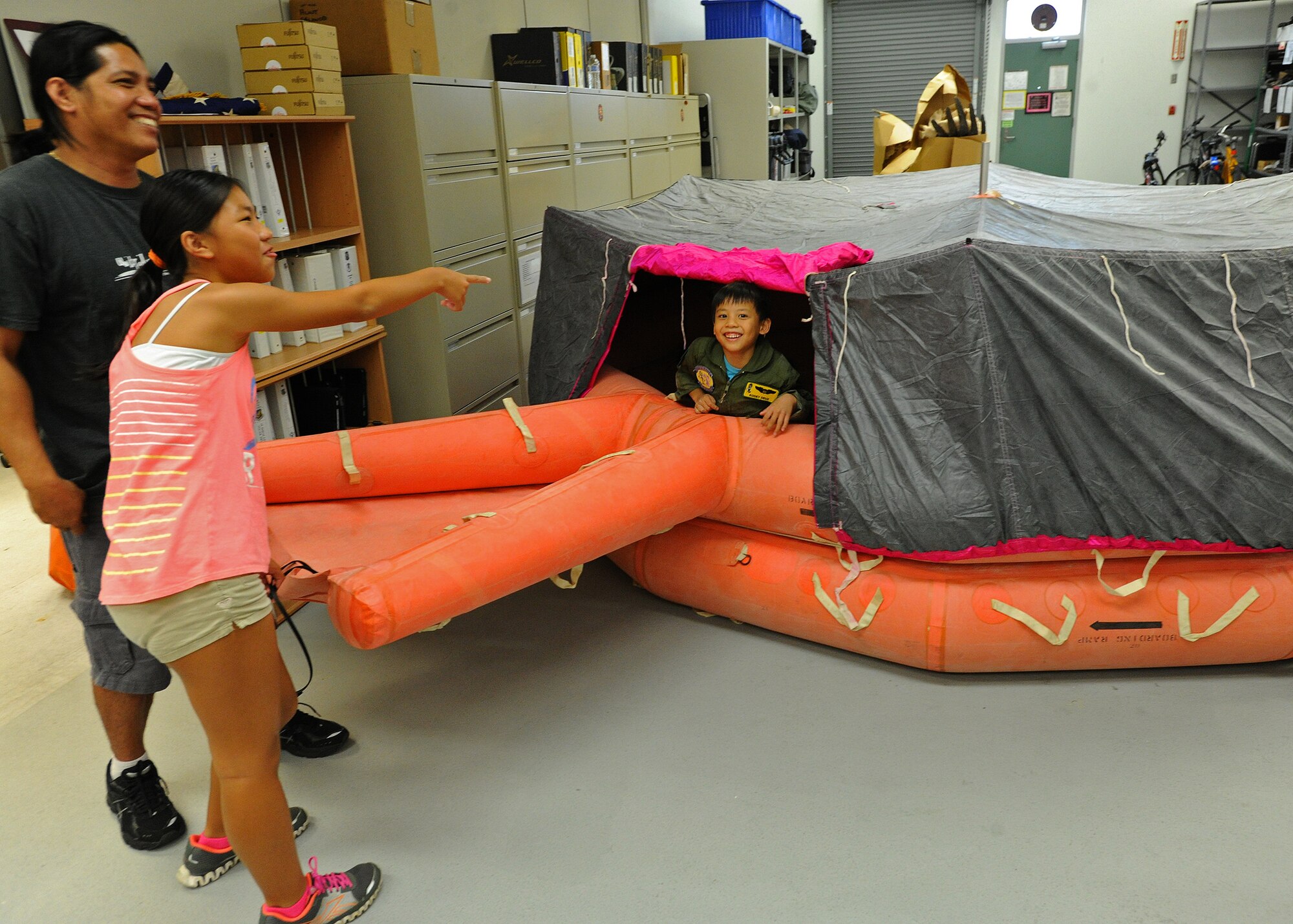 Kodey Deuz, a child battling aortic stenosis, aortic insufficiency and mitral regurgitation, right, hops around inside a 20-man inflatable life raft as sister, Kelci, and his father, Leo, and look on during a tour of the 15th Operations Support Squadron, aircrew flight equipment facility as part of the Pilot for a Day program at Joint Base Pearl Harbor-Hickam, Hawaii, Oct. 4, 2013. The goal of this program is to benefit children and their families in the local community who have catastrophic illnesses. It is not directed at any one illness or disease, and not restricted to children with "terminal" illnesses. For many children with catastrophic, but not "terminal" illnesses, the Pilot for a Day Program can be a significant part of their recovery. (U.S. Air Force photo/Tech. Sgt. Jerome S. Tayborn)