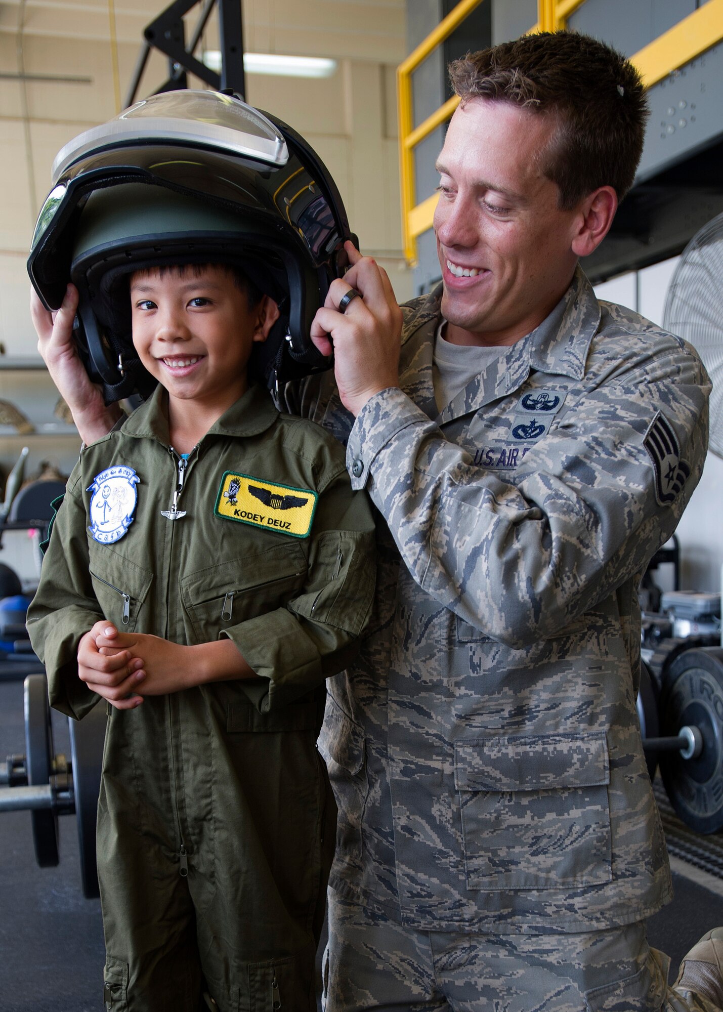 Kodey Deuz, a child battling aortic stenosis, aortic insufficiency and mitral regurgitation, trys on a bomb suit helmet with the help of Staff Sgt. Allen Middaugh, a 647th Civil Engineer Squadron explosives ordinance craftsman, as he poses for pictures at the 647th Civil Engineer Squadron, Explosive Ordnance Disposal work center shortly after touring the facility, as part of the Pilot for a Day program at Joint Base Pearl Harbor-Hickam, Hawaii, Oct. 4, 2013. The "Pilot for A Day" private organization invites children of all ages, military or civilian, to be guests of the 15th Wing and one of its flying squadrons for an entire day. In so doing, the goal is to give each child a special day and a break from whatever challenges they may be facing.  (U.S. Air Force photo/Tech. Sgt. Jerome S. Tayborn)