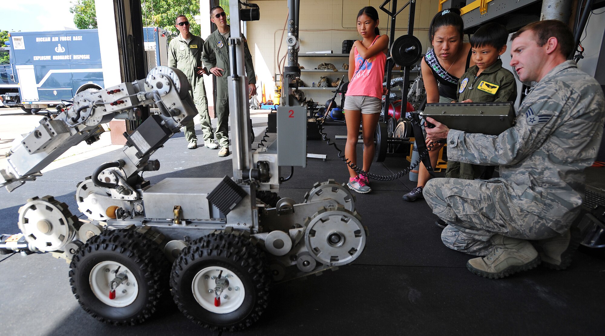 Kodey Deuz, a child battling aortic stenosis, aortic insufficiency and mitral regurgitation, center, operates a bomb robot with the help of Senior Airman Ben Hancock, 647th Civil Engineer Squadron munitions journeyman, right, as his mother Alicia and sister Kelci, left, look on, as part of the Pilot for a Day program at Joint Base Pearl Harbor-Hickam, Hawaii Oct. 4, 2013. Kodey was recommended for the program which aims to benefit children in the local community suffering from serious or chronic illnesses. (U.S. Air Force photo/Tech. Sgt. Jerome S. Tayborn)