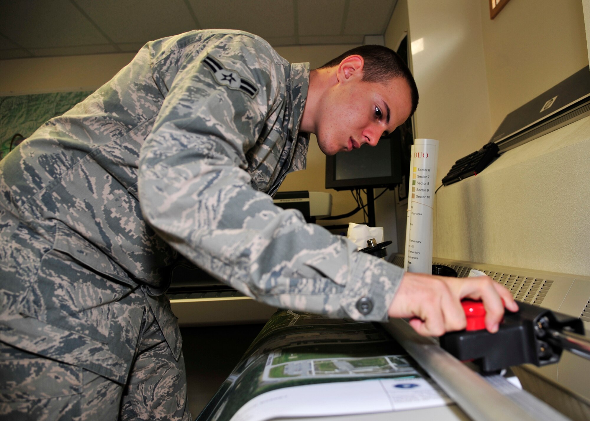 Airman 1st Class William Harper, 354th Civil Engineer Squadron GeoBase flight engineering assistant, trims a map for a customer Oct. 3, 2013, Eielson Air Force Base, Alaska. In support of the recent Operational Readiness Inspection, the GeoBase team provided geospatial intelligence and reproduced more than 200 hard copy maps for Icemen to access. (U.S. Air Force photo by Senior Airman Ashley Nicole Taylor/Released)