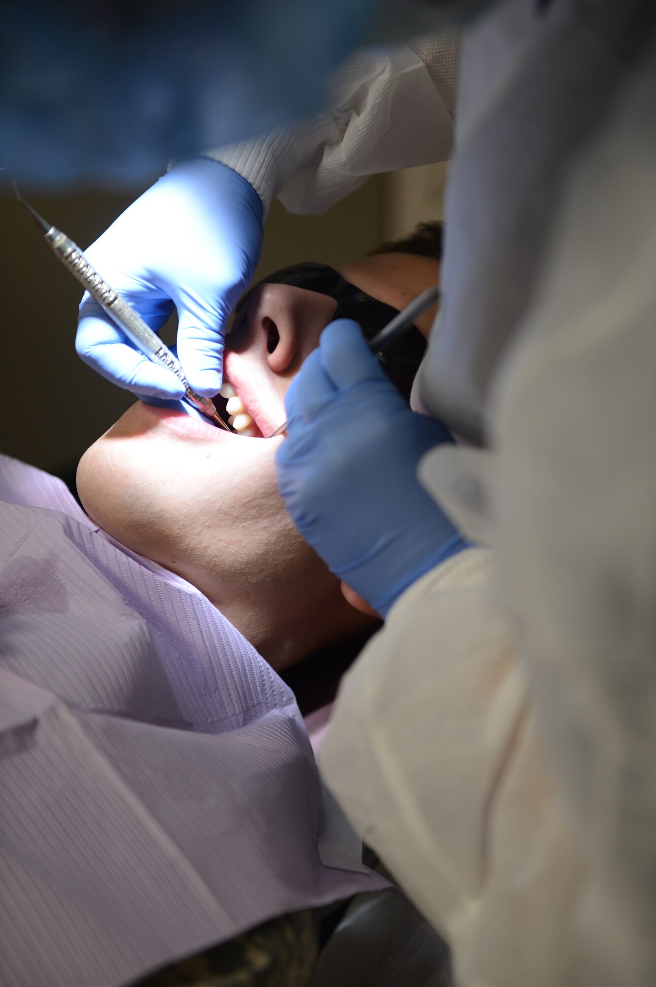 Staff Sgt. Tonya Collett, 20th Dental Squadron dental technician, pulls out plaque remains with a pick after using a cavitron to clean the teeth of Senior Airman Colin Casey, 20th DS lab technician, at Shaw Air Force Base, S.C., Sept. 30, 2013. A cavitron is an ultrasonic tool that uses water vibrations to break apart plaque. (U. S. Air Force photo by Airman 1st Class Krystal M. Jeffers/Released)