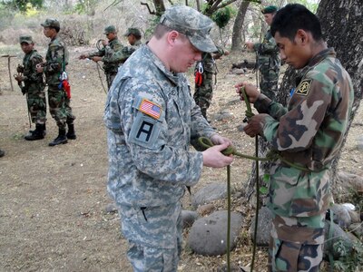 New Hampshire Army National Guard Staff Sgt. Derek Downey teaches a soldier from the new El Salvadoran Mountain Commando Unit how to build a rope harness, part of basic fixed rope installation and mountain casualty evacuation procedures in Morazan, El Salvador, Mar.20, 2012.