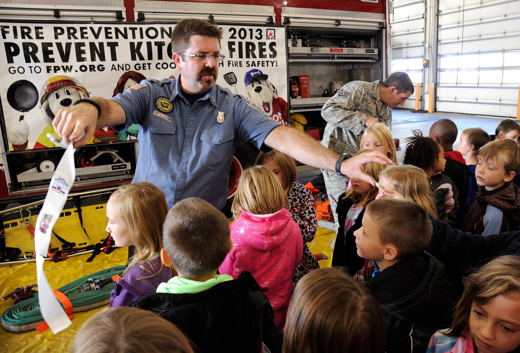 Craig Sayler, 92nd Civil Engineer Squadron fire fighter, hands out stickers to Michael Anderson Elementary school students at the Fire Department on Fairchild Air Force Base, Wash., Oct. 7, 2013. During Fire Prevention week, fire fighters teach people about the importance of having “two ways out” of a building and what they can do to prevent fires. (U.S. Air Force photo by Airman 1st Class Ryan Zeski/Released)