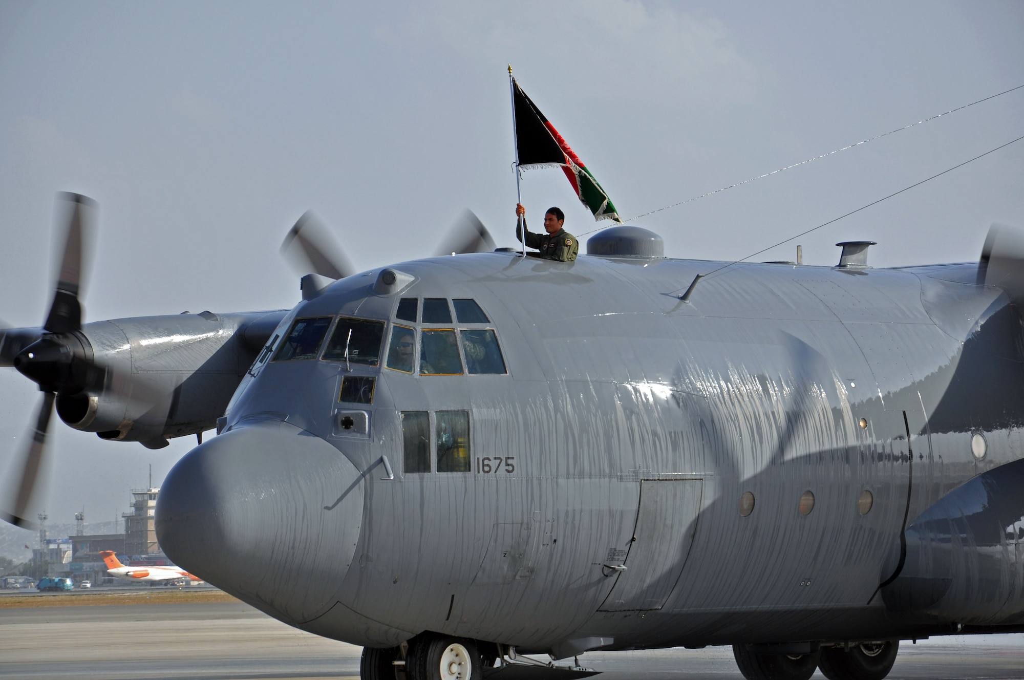 Afghan Air Force 1st Lt. Khial Shinwari, C-130 pilot, raises the Afghan flag as one of two of the newly delivered C-130H models to the AAF taxis onto the ramp during a ceremony Oct. 9, 2013 at Kabul International Airport, Afghanistan. Shinwari is one of the two first AAF C-130 pilots. Adding the C-130 to the AAF inventory provides medium airlift capabilities for the AAF, allowing for better range as well as increased passenger and cargo movement. The C-130H can cross the entirety of Afghanistan without refueling and can carry 10 times the amount of cargo of a Cessna 208, another aircraft in the AAF inventory. (U.S. Air Force photo/Capt. Anastasia Wasem)