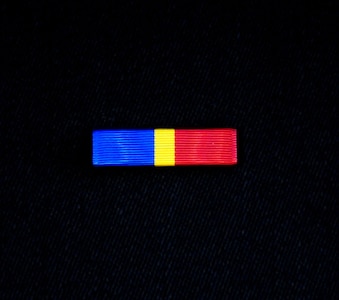 The Alaska National Guard State Partnership Program Ribbon is divided into three vertical sections of blue, gold and red, representing the significance of the partnership between Alaska and the Republic of Mongolia by representing the colors of each of their flags. The blue represents the eternal skies expanding above both nations, the red symbolizes progress and prosperity and the gold signifies wealth.