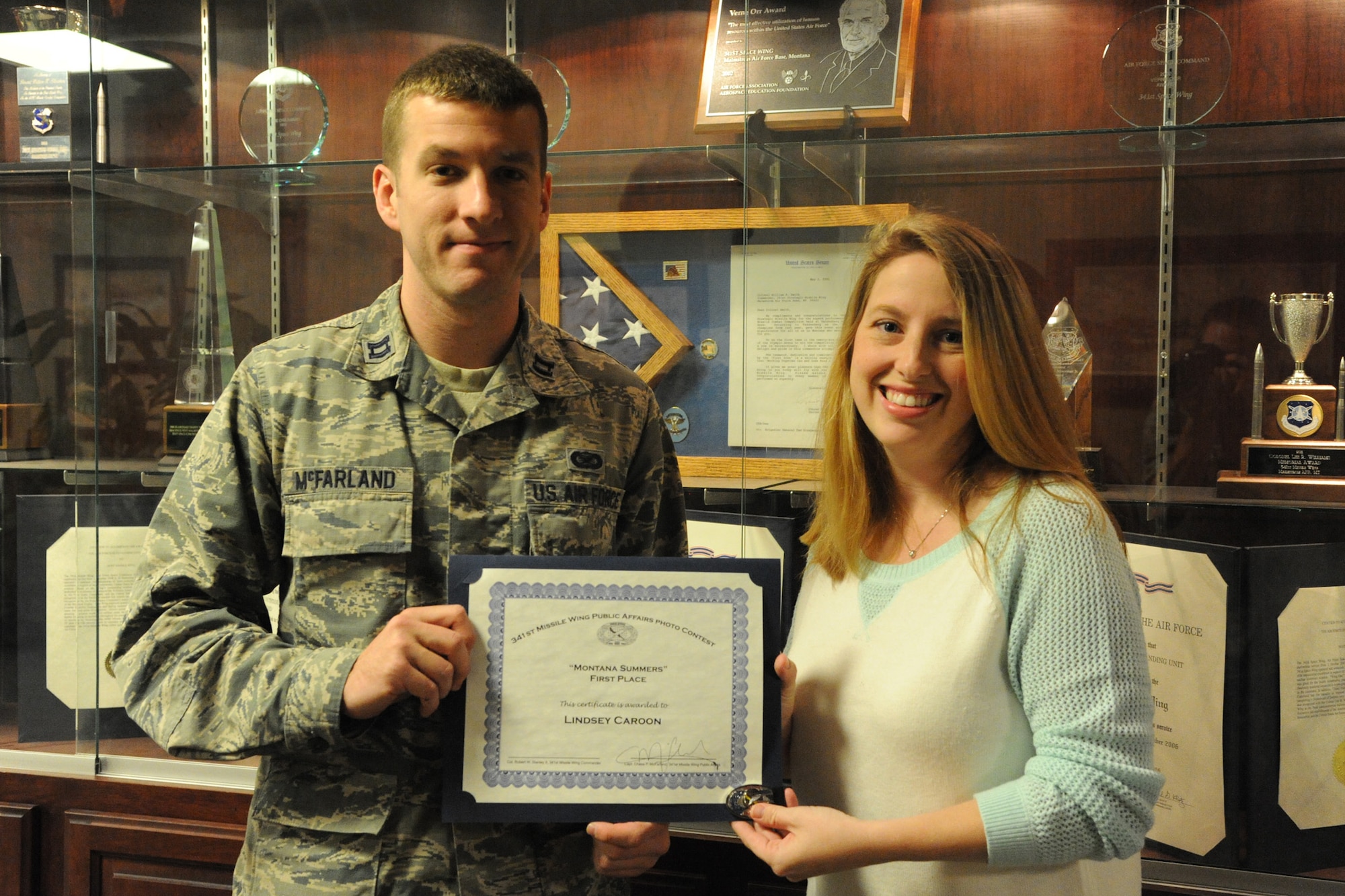 Lindsey Caroon, wife of Maj. Speight Caroon, 341st Operations Support Squadron ICBM emergency war orders chief, receives a certificate and coin from Capt. Chase McFarland, 341st Missile Wing Public Affairs deputy chief, after winning the 341st MW PA Quarterly Amateur Photo Contest on Oct. 9. Caroon’s photo of her children camping in Glacier National Park in Hungry Horse, Mont., expertly encompassed last quarter’s theme, “Montana Summers.” (U.S. Air Force photo/Airman 1st Class Collin Schmidt)