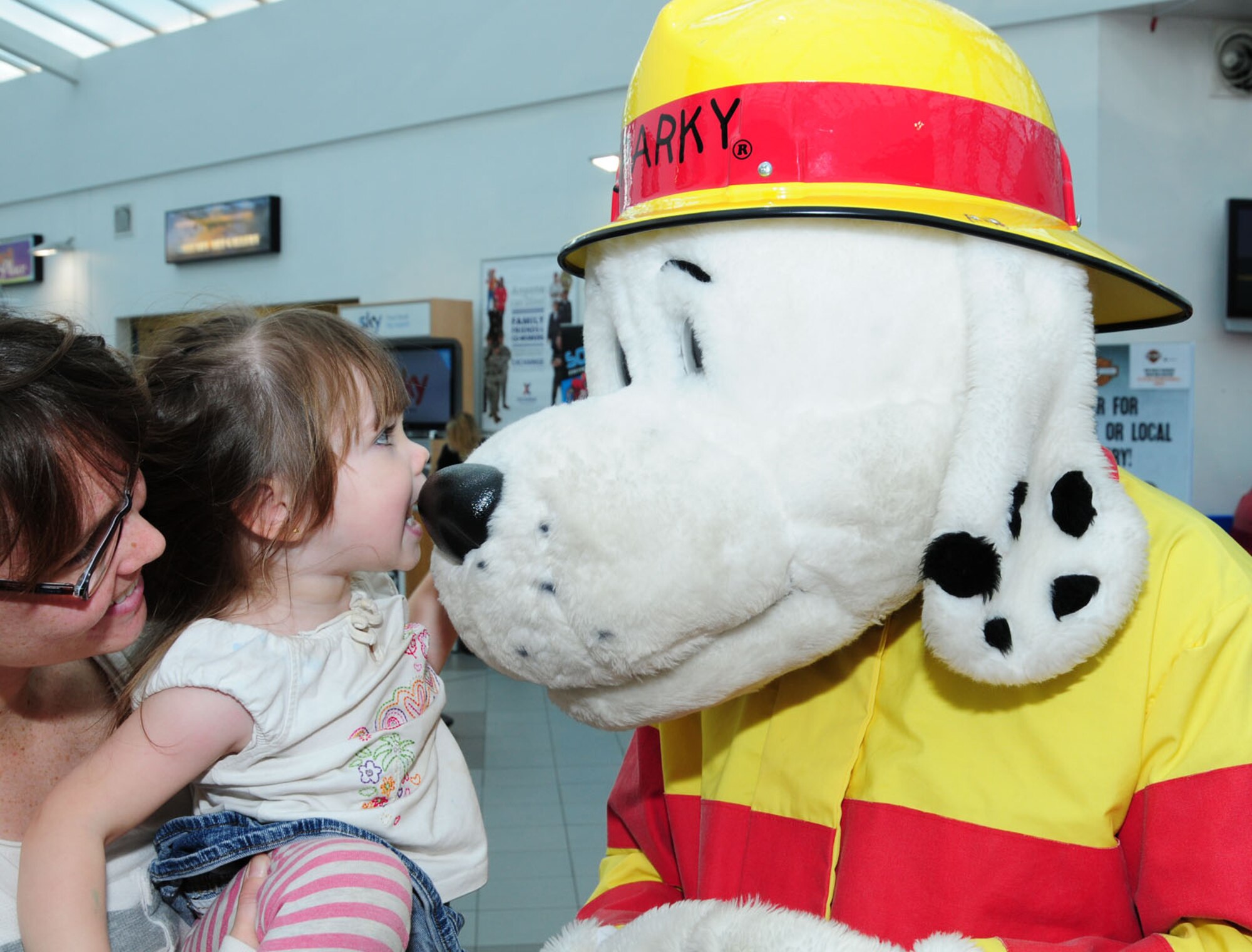 Honor Schmidt, center, 2, daughter of Staff Sgt. Jacob Schmidt, 352nd Special Operations Group, prepares to give Sparky the Fire Dog a kiss as mom, Toni Schmidt, from Clarksville, Tenn., watches Oct. 9, 2013, at the BXtra on RAF Mildenhall, England. Sparky greeted children and Team Mildenhall members at the BXtra as part of Fire Prevention Week. (U.S. Air Force photo by Karen Abeyasekere/Released)