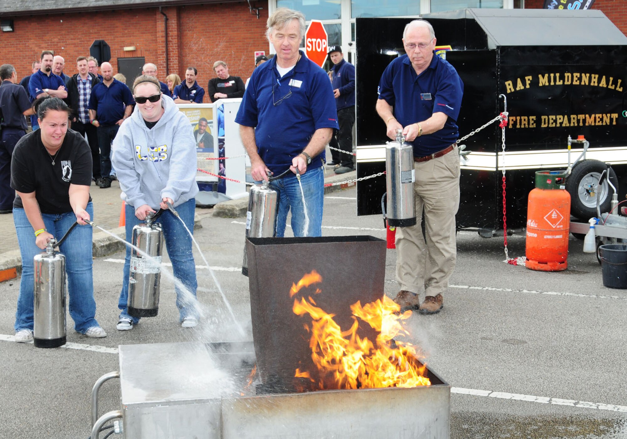 Employees from Army and Air Force Exchange Service facilities try their hand at extinguishing a fire Oct. 8, 2013, as part of a training session during Fire Prevention Week on RAF Mildenhall, England. Firefighters from the 100th Civil Engineer Squadron Fire Department fire prevention office demonstrated how to correctly and safely put out a fire with an extinguisher, along with a grease pan fire in the home. Other events included a free and a fire muster challenge. (U.S. Air Force photo by Karen Abeyasekere/Released)