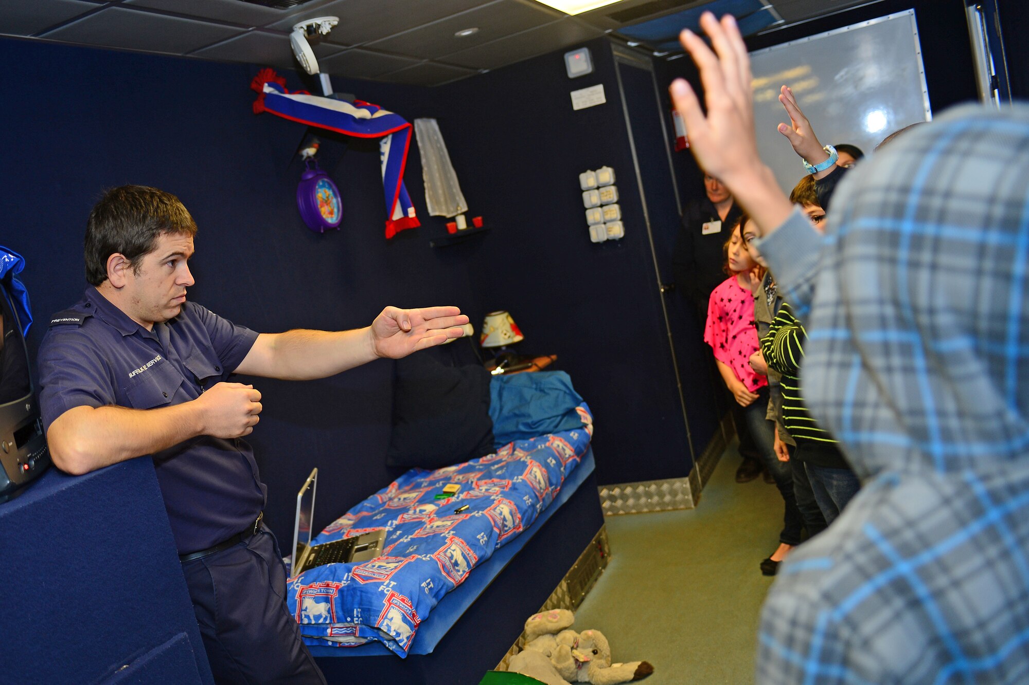 Aaron Tooke, Suffolk Fire and Rescue Service youth development specialist officer, helps fourth grade students from the intermediate school at Royal Air Force Lakenheath, England, identifiy fire safety hazards in a mobile fire simulation trailer Oct. 8, 2013. Firefighters from the Suffolk Fire and Rescue Service worked with 48th Civil Engineering Squadron firefighters to help raise awareness about fire safety as a part of National Fire Prevention Week. (U.S. Air Force photo by Airman 1st Class Dana J. Butler/Released)