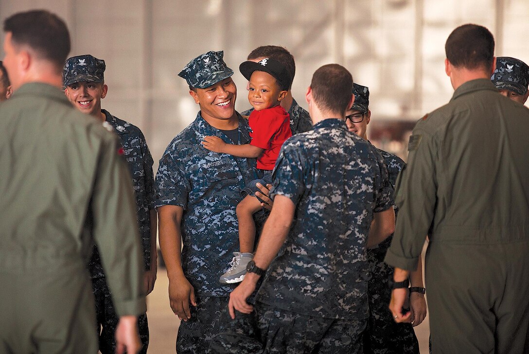 Petty Officer 2nd Class Juan Rogers, aviation structural mechanic, carries his son while chatting with fellow sailors at Helicopter Maritime Strike Squadron 37’s homecoming ceremony, Oct. 8, 2013. Rogers was among the sailors in the detachment returning home from more than 180 days of training overseas. (U.S. Marine Corps photo by Lance Cpl. Janelle Y. Villa)