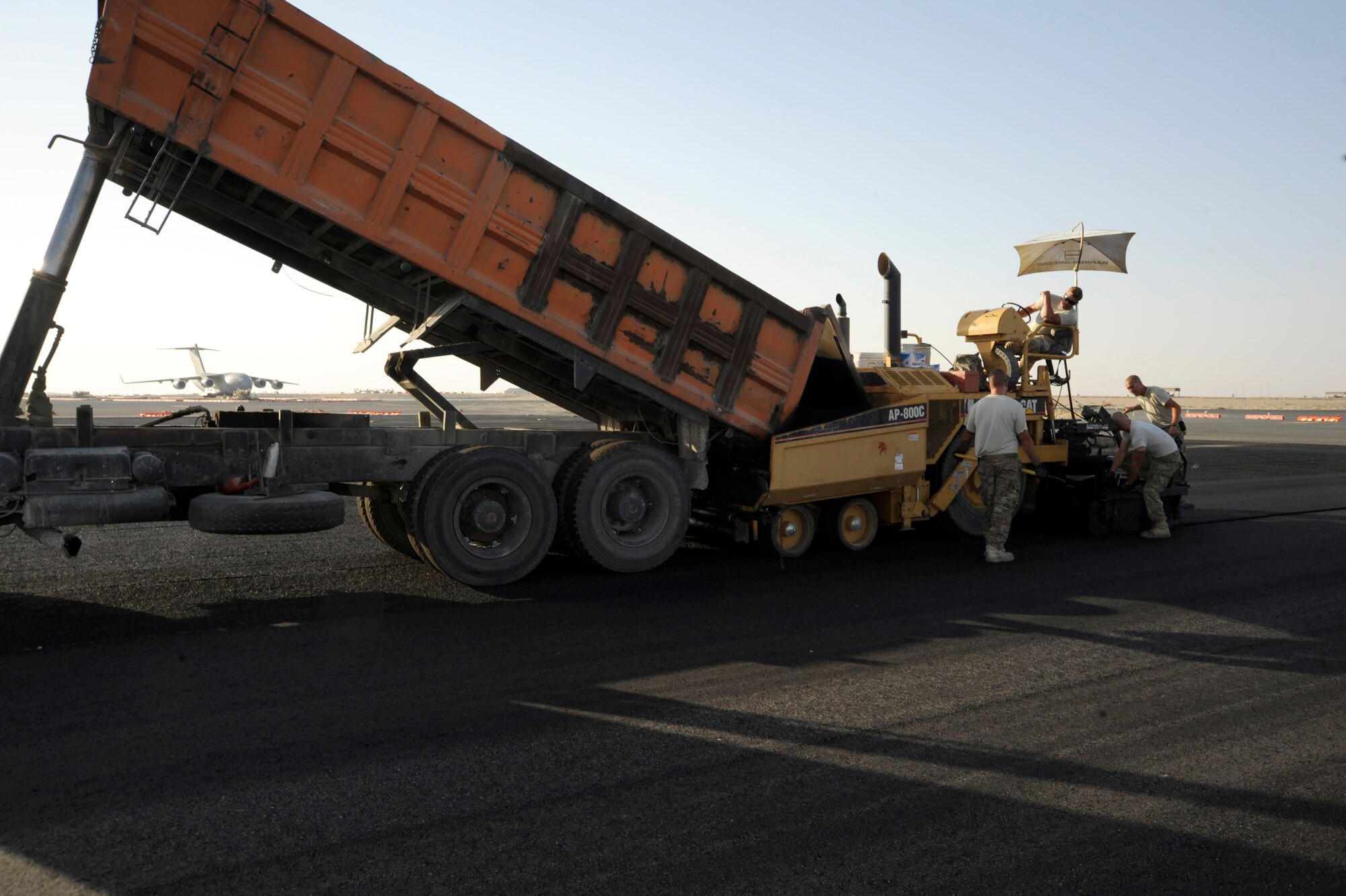 Members of the 557th Expeditionary Red Horse Squadron work together using an asphalt paver here, Oct. 4, 2013.  The new asphalt will be a needed upgrade for an aircraft parking area.  This project has taken three months and is projected to use 2,763 metric tons of asphalt to complete. (U.S. Air Force photo by Master Sgt. Christopher A. Campbell)