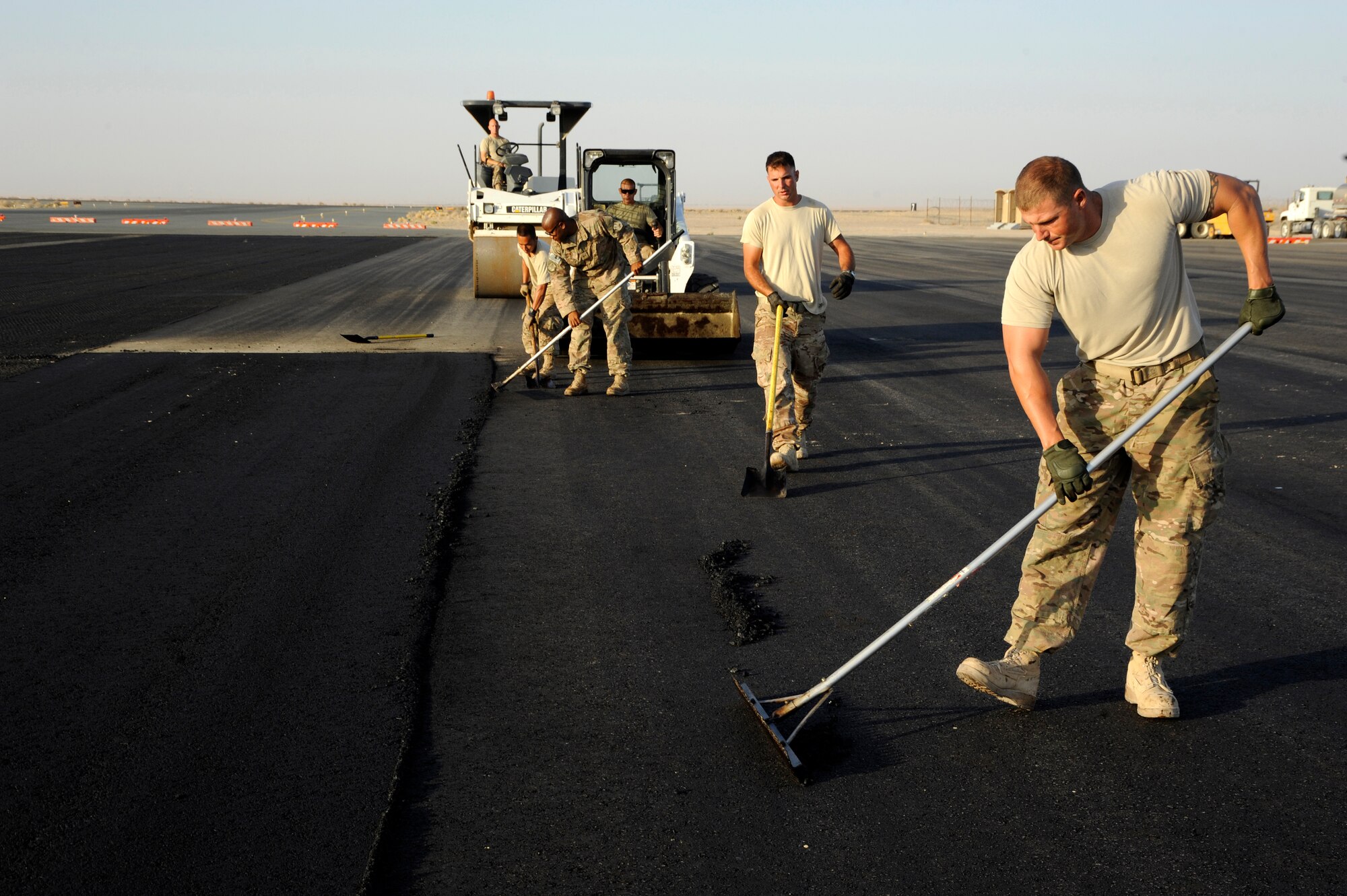 Members of the 557th Expeditionary Red Horse Squadron work together to level out new asphalt here, Oct. 4, 2013.  The members are using lutes and shovels to level the asphalt and clear away excess to prepare the area before the rollers compact it.  This team has worked on this project since mid-August to tear up the old asphalt and get the area ready for six aircraft parking spots for the 386th Air Expeditionary Wing. (U.S. Air Force photo by Master Sgt. Christopher A. Campbell)