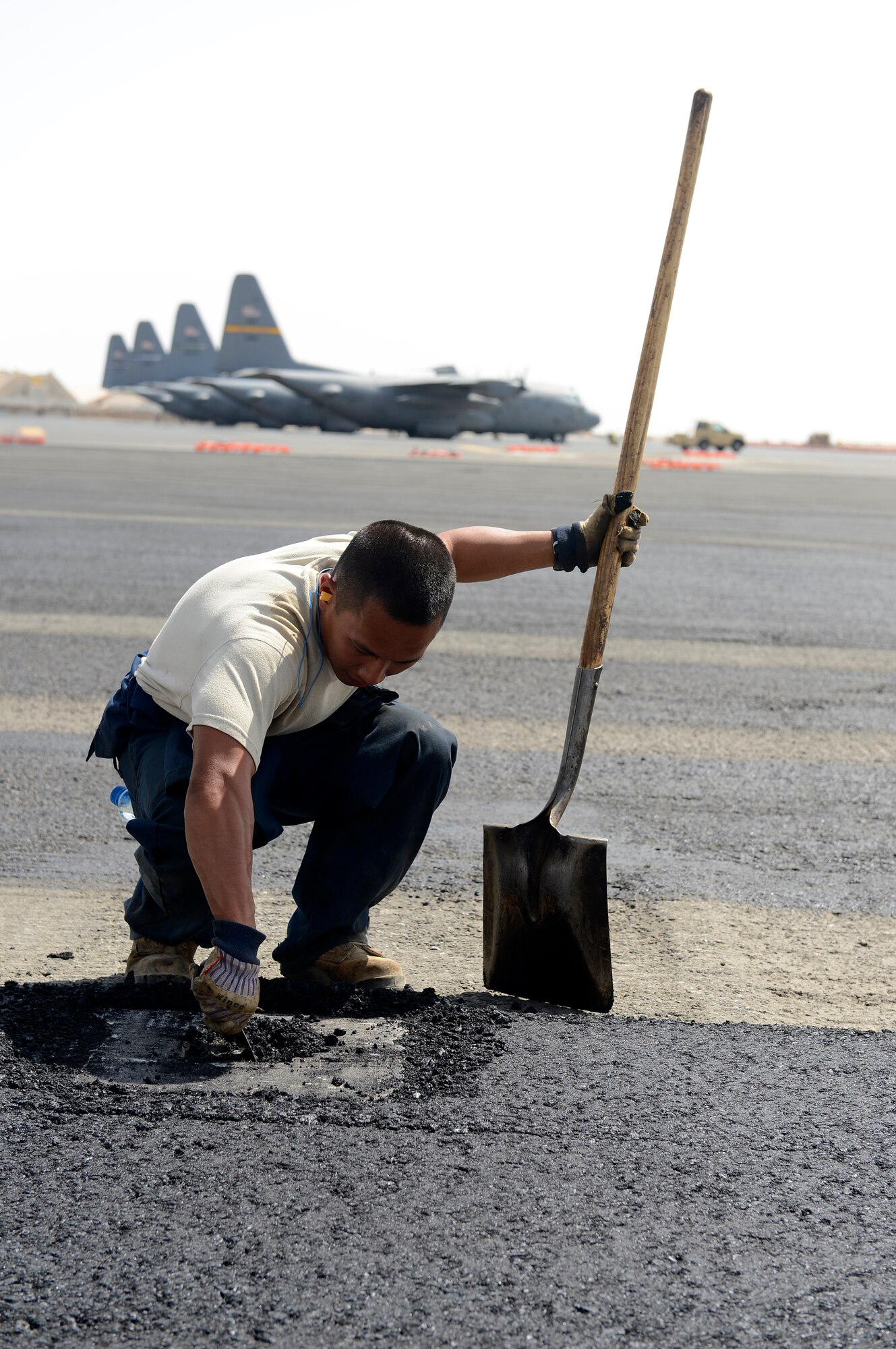 Senior Airman Phan Vu, 557th Expeditionary Red Horse Squadron, heavy equipment operator, scrapes away asphalt here, Oct. 3, 2013.  Vu is clearing out asphalt from the anchors on the new flight line aircraft parking area.  Vu, a native of Delray Beach, Fla., is deployed out of Malmstrom Air Force Base, Mont. (U.S. Air Force photo by Master Sgt. Christopher A. Campbell)
