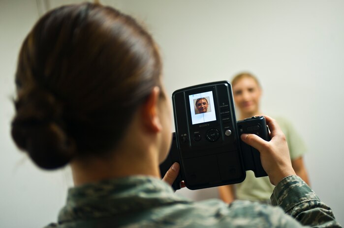 Staff Sgt. Melissa Thomas, 99th Force Support Squadron formal training and passports NCO in charge, takes a passport photo of Senior Airman Analise Sylvester, 99th FSS customer service technician, at the military customer service office Oct. 11, 2013, at Nellis Air Force Base, Nev. A two by two inch photo, which is provided by the customer service office at the military personnel section, is required for processing an official passport application. (U.S. Air Force photo by Staff Sgt. Michael Charles)