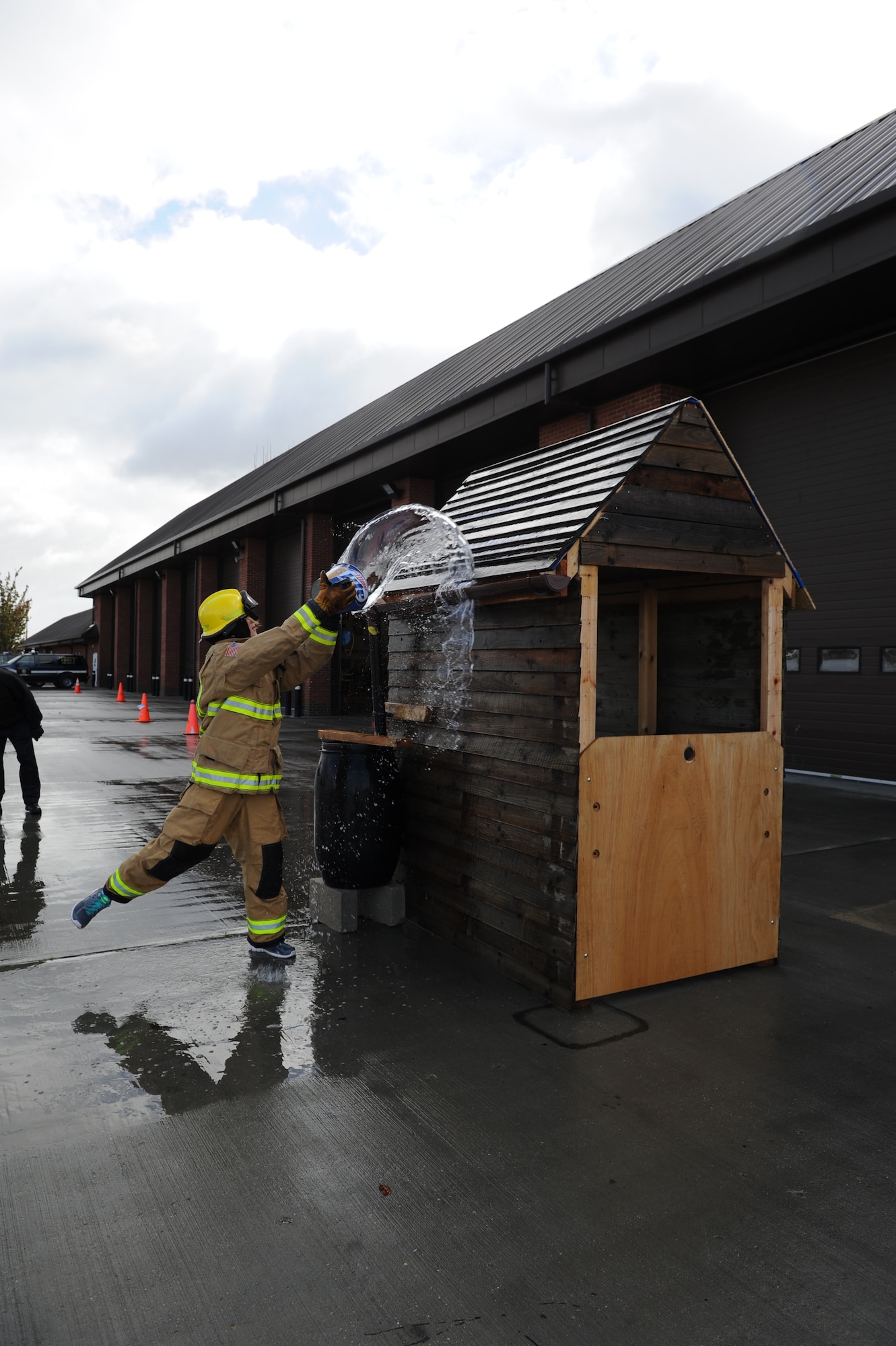 U.S. Air Force Senior Airman Laura Yahemiak, 100th Air Refueling Wing Public Affairs broadcaster, throws water on the roof of a simulated burning building during the third annual Fire Muster Oct. 10, 2013, on RAF Mildenhall, England. Team Mildenhall members grouped together to compete for first place. Yahemiak performed a number of firefighter-themed tasks while participating in the fire muster. (U.S. Air Force photo by Airman 1st Class Preston Webb/Released)