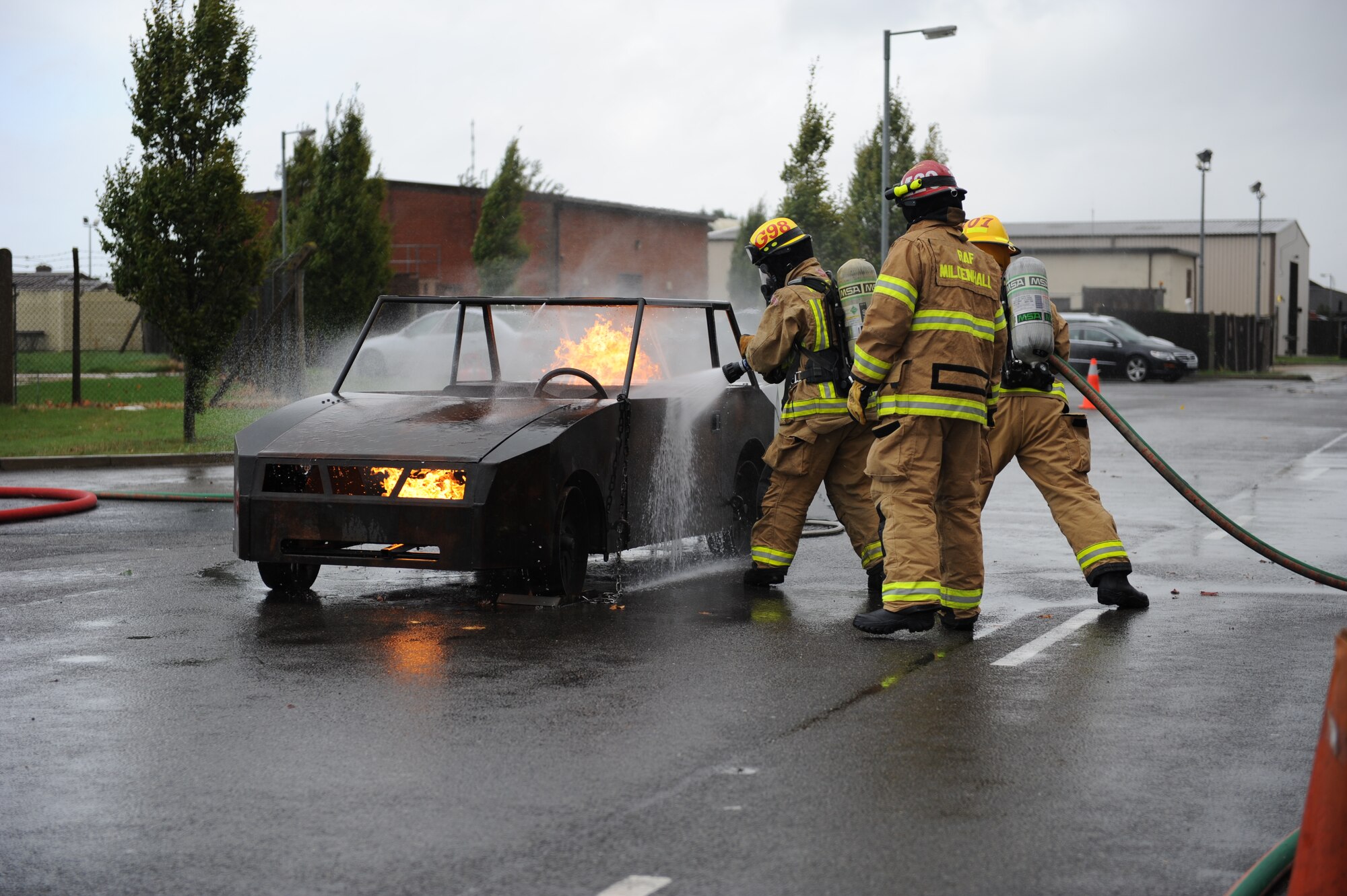 Firefighters from the 100th Civil Engineer Squadron Fire Department extinguish a flaming car before the third annual Fire Muster Oct. 10, 2013, on RAF Mildenhall, England. During the muster, Team Mildenhall members completed several firefighter-themed tasks such as a hose roll, dummy drag and a hose assembly. Eight teams competed against each other during the fire muster. (U.S. Air Force photo by Airman 1st Class Preston Webb/Released)