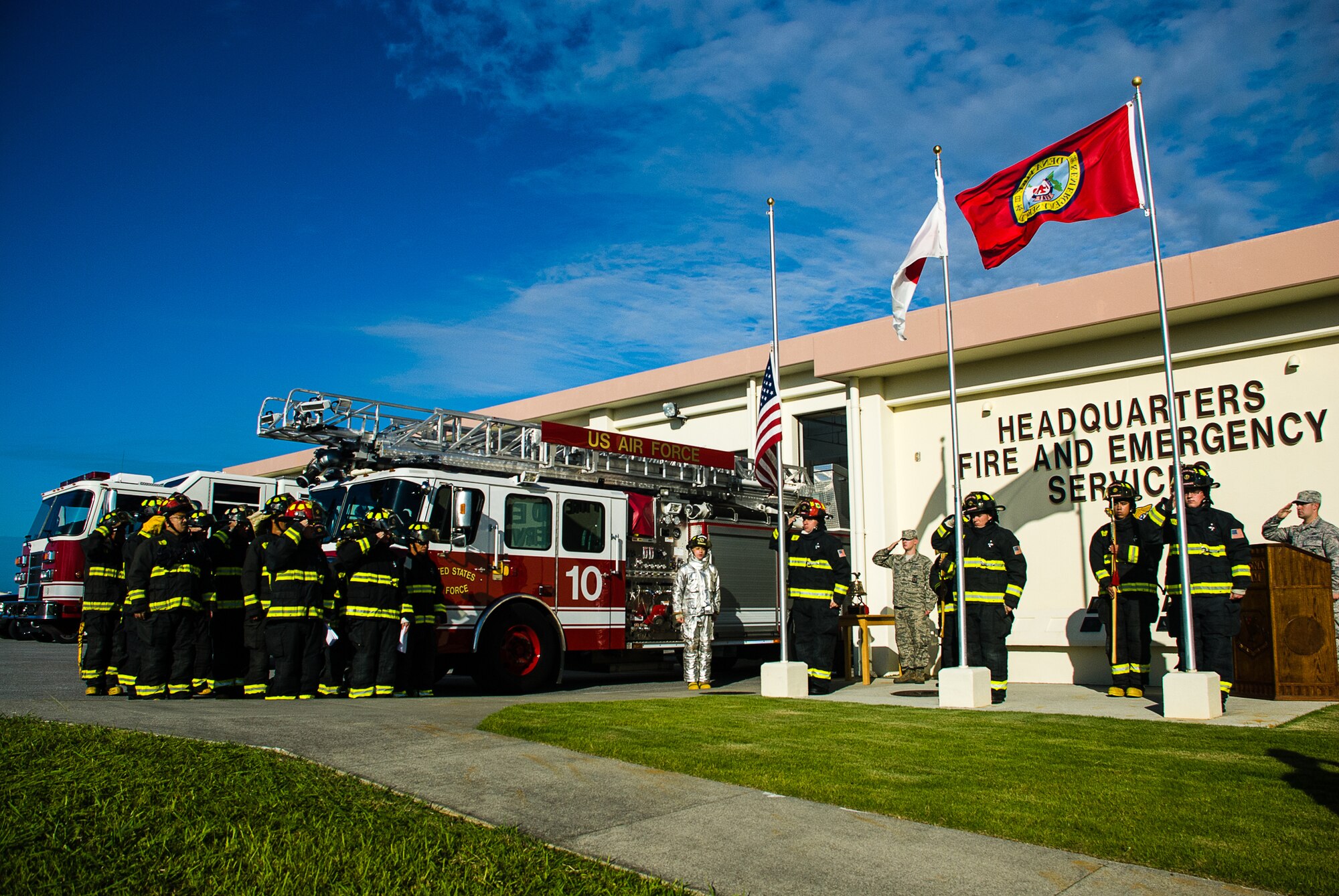 U.S. Air Force Staff Sgt. Michael Collard (center), 18th Civil Engineer Squadron firefighter, sings the national anthems of Japan and the United States as fellow firefighters salute the flags during a Bells Across America ceremony Oct. 11, 2013, on Kadena Air Base, Japan. Bells Across America is a remembrance ceremony observed annually to honor fallen firefighters. (U.S. Air Force Staff Sgt. Alexy Saltekoff)