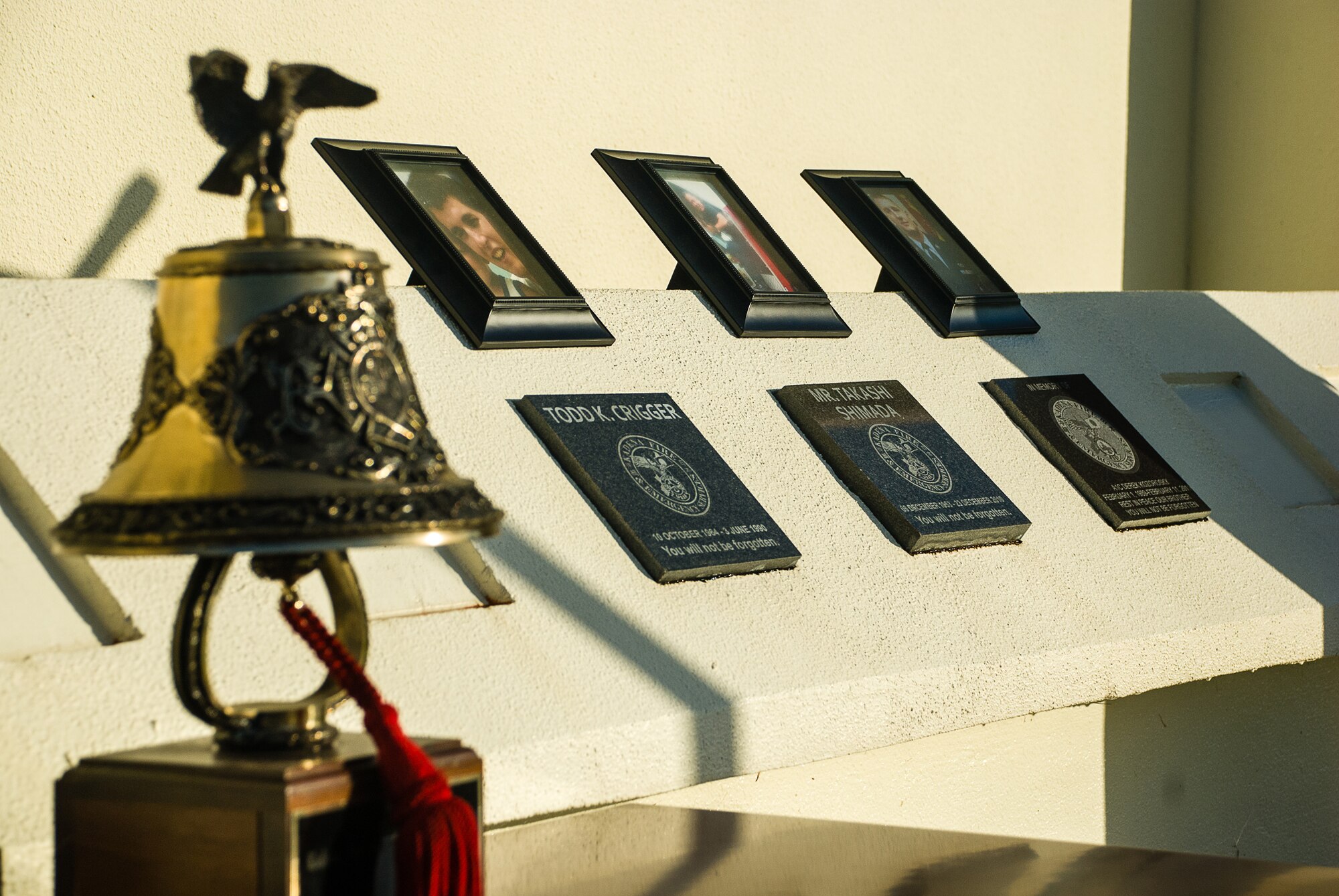 Pictures rest above the markers for Kadena’s fallen firefighters Todd Crigger, Takashi Shimada and Derek Kovorosky on the memorial outside Headquarters, Fire Emergency Services during the Bells Across America ceremony Oct. 11, 2013, on Kadena Air Base, Japan. This was the third annual Bells Across America, a nation-wide remembrance ceremony. (U.S. Air Force Staff Sgt. Alexy Saltekoff)