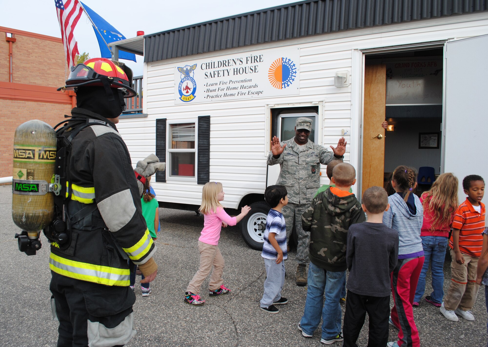 Staff Sgt. Aaron Coleman, Grand Forks Air Force Base fireman, gives high fives to students for successfully completing a fire drill out of the Children’s Fire Safety House Oct. 8, 2013, at Eielson Elementary School at Grand Forks AFB, N.D. The Children’s Fire Safety House is a trailer used by the base fire department designed to teach children E.D.I.T.H., which stands for Exit Drills In The Home. The fire drills were part of several activities that took place during this year’s Fire Prevention Week. (U.S. Air Force photo/Staff Sgt. Luis Loza Gutierrez) 
