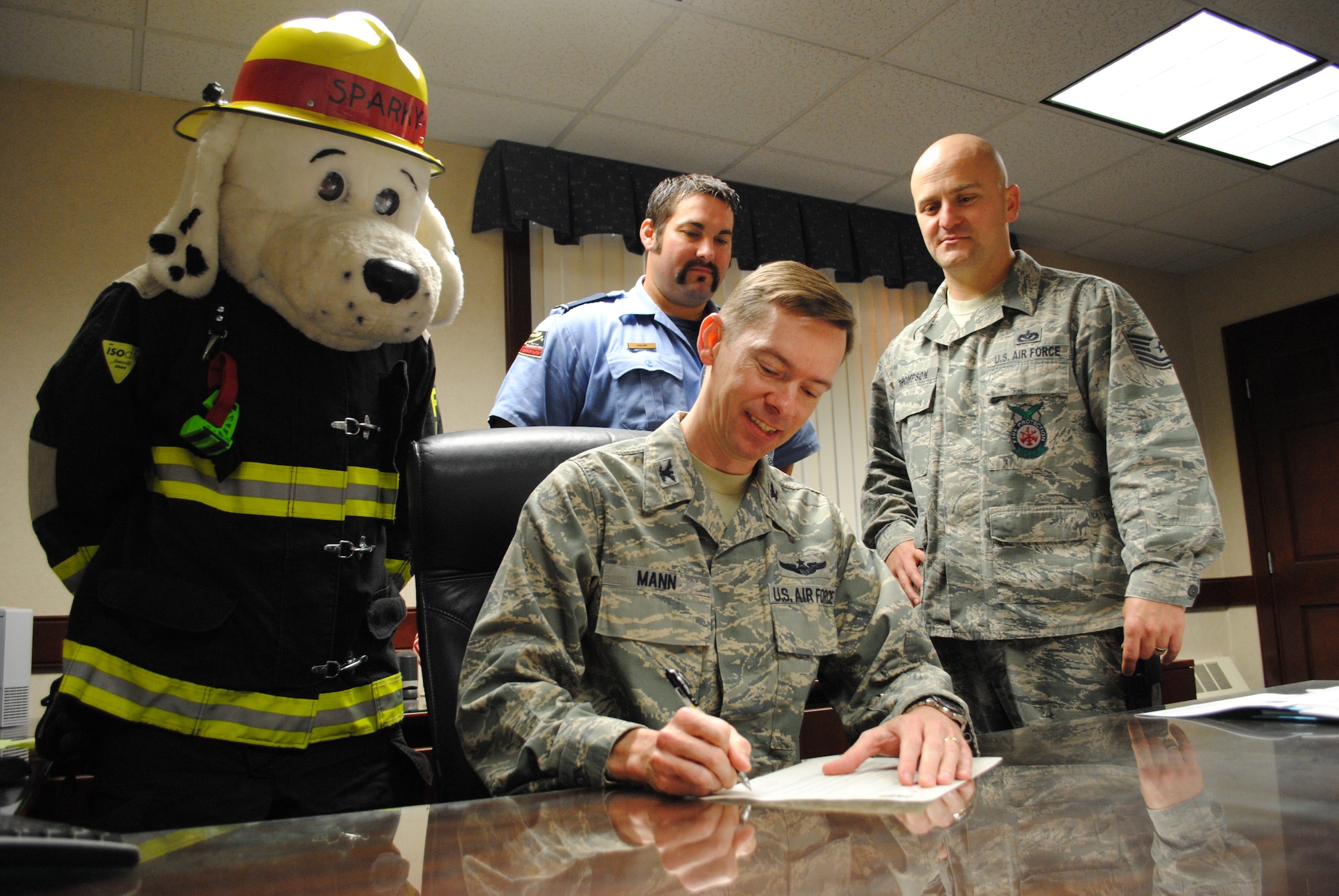 Sparky the Fire Prevention Mascot, Justin Haskamp and Tech. Sgt. Joshua Thompson from the 319th Civil Engineer Squadron fire department, witness Col. Christopher Mann, 319th Air Base Wing vice commander, sign the 2013 Fire Prevention Week proclamation on Oct. 7, 2013, at the 319th ABW headquarters building. The signing of the proclamation official kicked off the base’s fire prevention week events, which took place Oct. 7-11. (U.S. Air Force photo/Staff Sgt. Luis Loza Gutierrez) 
