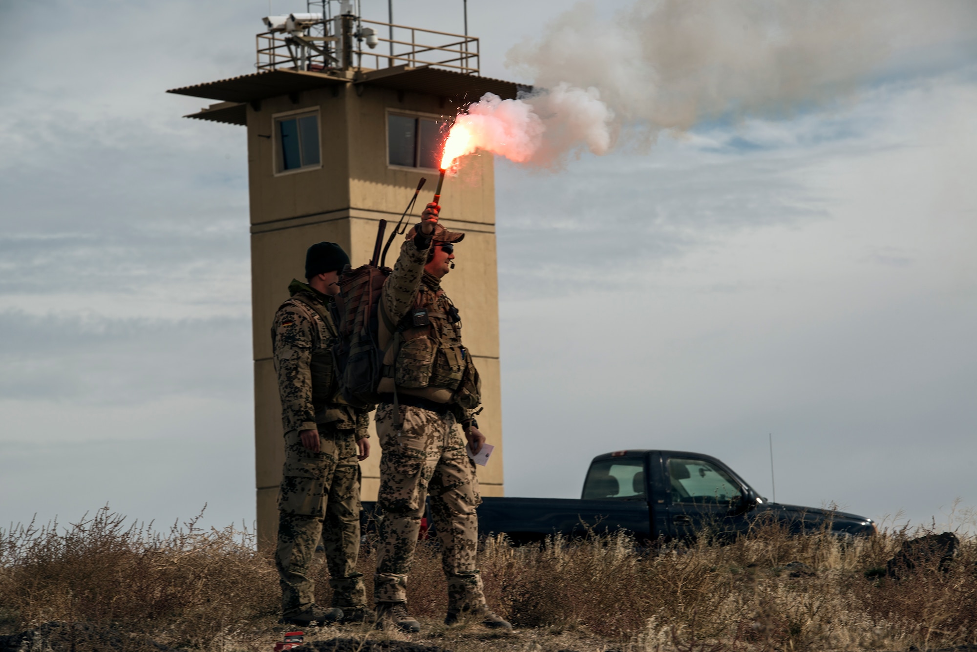 German Air Force 1st Lt. Tim Ermisch, joint terminal attack controller, holds an indicator flare as he and fellow GAF JTAC 1st Lt. Fabian Rauscher await a low-passing show of force from two U.S. Air Force F-15E Strike Eagles from the 391st Fighter Squadron during exercise Mountain Roundup 2013, at Saylor Creek bombing range near Mountain Air Force Base, Idaho, Oct. 16, 2013. “JTACs can use a show of force just as a psychological deterrent for the enemy, but if that doesn't work, you often have to go kinetic,” said Ermisch. (U.S. Air Force photo by Master Sgt. Kevin Wallace/RELEASED)