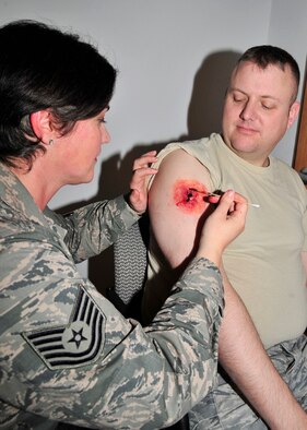 Tech. Sgt. Crystal St. Denis, 354th Medical Group NCO in charge of moulage, creates a simulated gunshot wound on Master Sgt. David Herron, 354th MDG dental flight chief, Oct. 2, 2013, Eielson Air Force Base, Alaska. St. Denis’ favorite part of all the injuries she creates is watching the reactions of the people responding. (U.S. Air Force photo by Senior Airman Ashley Nicole Taylor/Released)