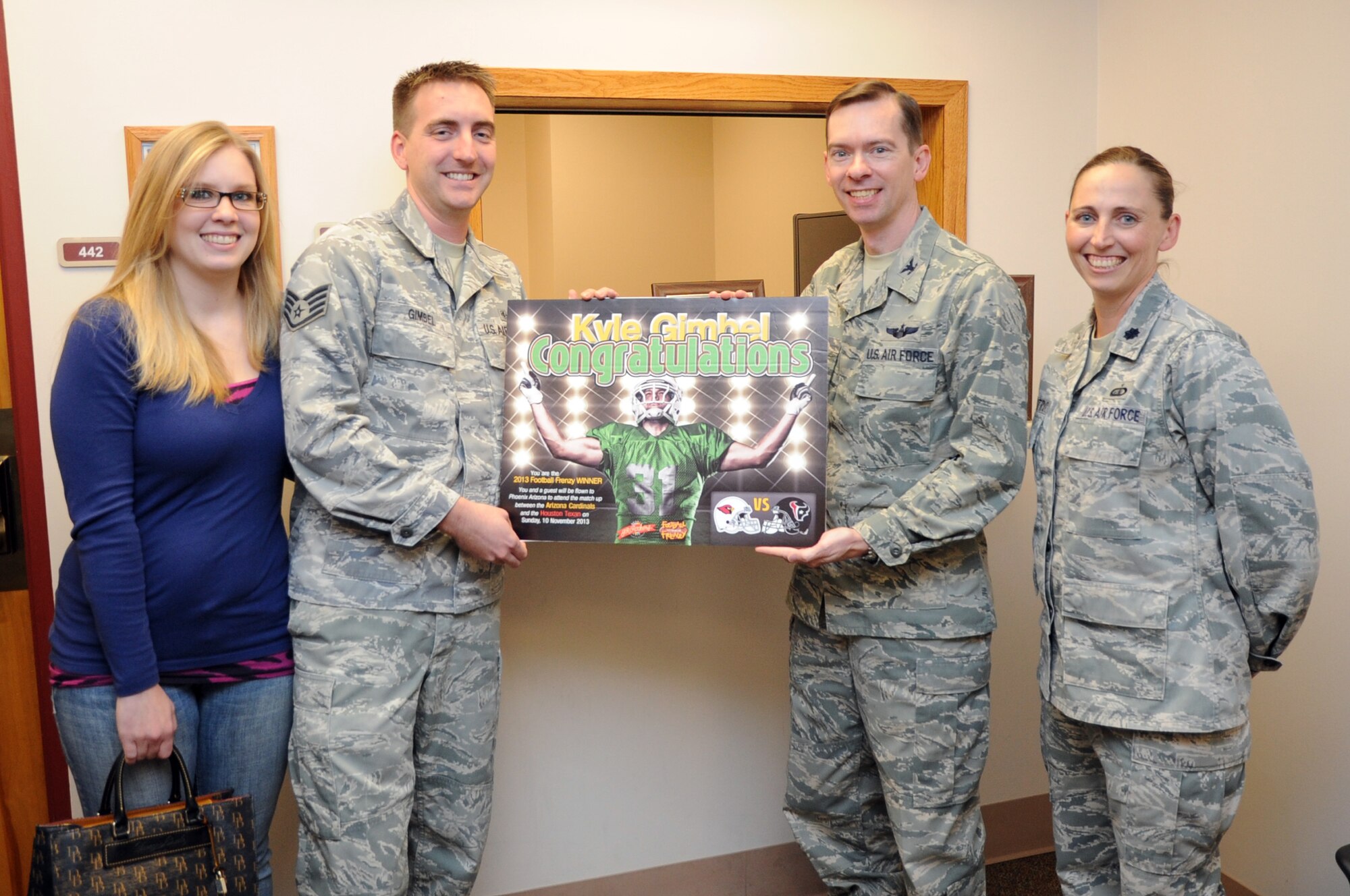 Staff Sgt. Kyle Gimbel, 319th Medical Support Squadron radiology technician, and his wife, Cassandra, are presented with the grand prize in the 2013 Football Frenzy contest by Col. Christopher Mann, 319th Air Base Wing vice commander, and Lt. Col. Regina Castro, 319th Force Support Squadron commander. The Gimbels will receive two free tickets to an NFL game pitting the Arizona Cardinals against the Houston Texans. (U.S. Air Force photo by Staff Sgt. David Dobrydney)