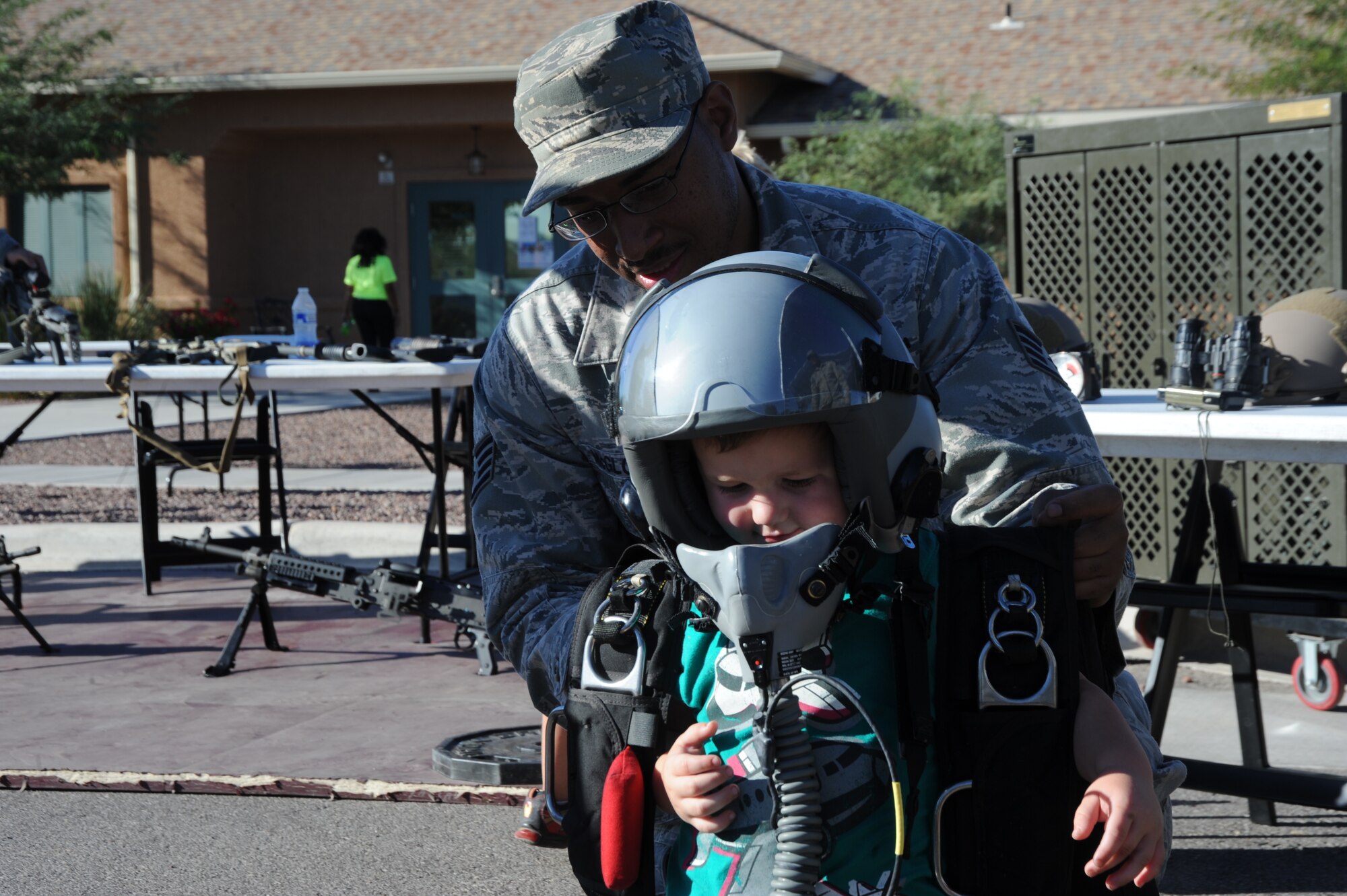 U.S. Air Force Staff Sgt. Fernandis McGlothin, 48th Rescue Squadron aircrew flight equipment technician, helps a child put on a flight harness during the National Night Out at Davis-Monthan Air Force Base, Ariz., Oct. 1, 2013. National Night Out heightens crime and drug prevention awareness as well as generates support for local anti-crime efforts. (U.S. Air Force photo by Senior Airman Sivan Veazie/Released) 