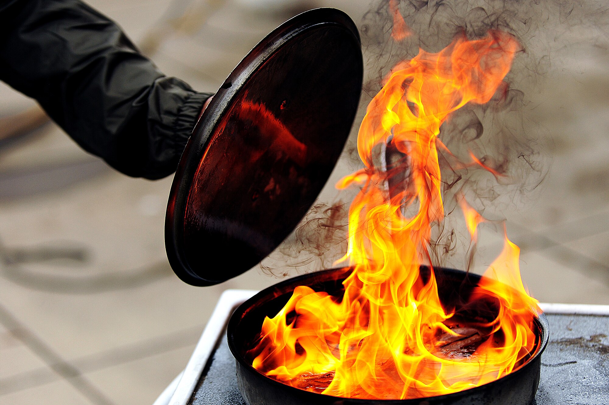 A volunteer tests their ability to put out a grease fire during a demonstration as part of Fire Prevention Week at Seymour Johnson Air Force Base, N.C. Oct. 11, 2013.  According to Eric Harper, 4th Civil Engineer Squadron lead fire inspector, the best way to put out a stove fire is to use the lid as a shield to cover the flames and then turn off the source of heat.  (U.S. Air Force photo by Airman 1st Class Brittain Crolley)