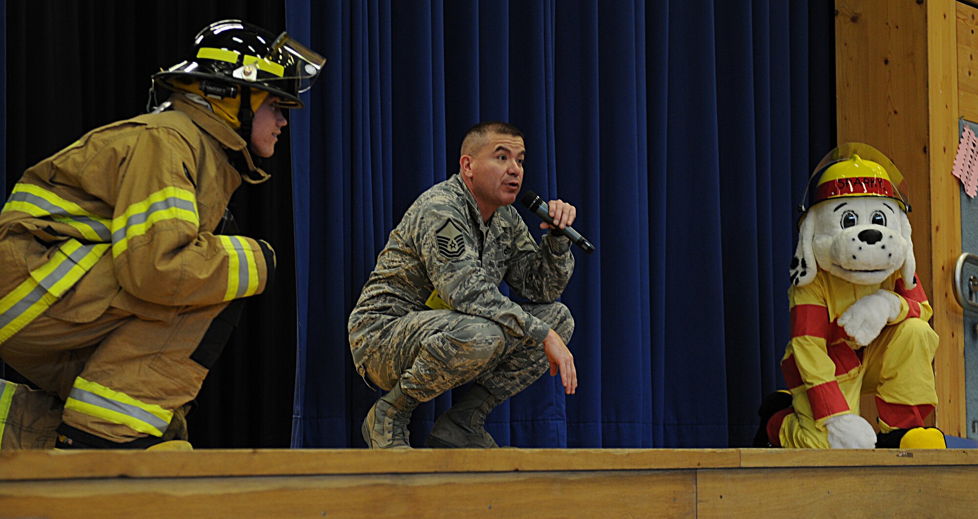 Airman 1st Class Brice Haylett, 86th Civil Engineer Squadron firefighter, Master Sgt. Paul Luevano, 86th CES assistant chief of fire prevention, and Sparky the fire dog demonstrate how to crouch down when there is a fire in the room during Fire Prevention Week, Oct. 7, 2013, Ramstein Air Base, Germany. Sparky and KMC firefighters held briefings and conducted live fire extinguisher training at KMC elementary schools, the Ramstein Express gas station and Enlisted Club. (U.S. Air Force photo/Airman 1st Class Holly Mansfield)