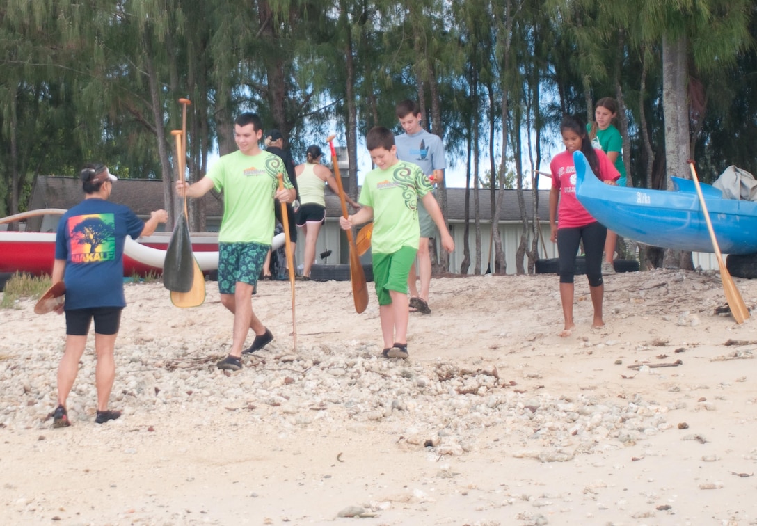 Several youth paddlers gather wooden paddles to use in a practice at Hale Koa Beach before launching their outrigger canoe, Oct. 14, 2013. Adults of any age and children 9 years old or older may participate in the club. (U.S. Marine Corps photo by Christine Cabalo)
