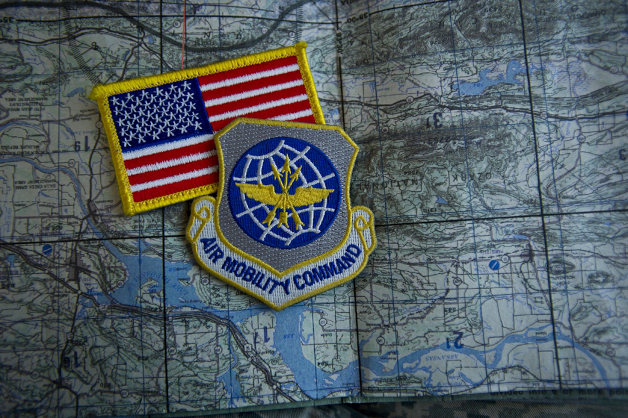 An American Flag and Air Mobility Command patch lay on a land navigation and evasion map Oct. 10, 2013, in Derby, Kan. Developed during World War II, these maps were used by many servicemen to escape from behind enemy lines. They include helpful information such as basic navigation routs and local plants and wildlife. This chart was used during mandatory survival, evasion, resistance and escape refresher training, given every three years for aircrew, where participants had to evade capture and navigate their way through the woods to specific points, including a simulated rescue point. (U.S Air Force photo/Senior Airman Katrina M. Brisbin)