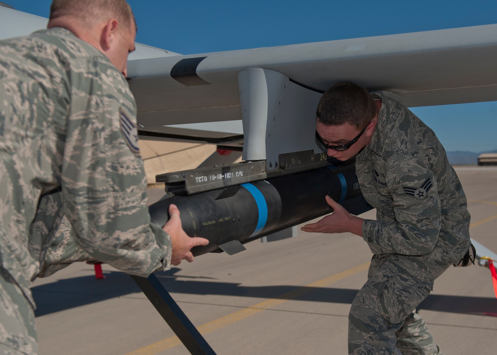 Staff Sgt. Asher Craig and Senior Airman Edward Smigiel, 849th Aircraft Maintenance Squadron weapons load crew, load an inert missile during the quarterly load crew competition at Holloman Air Force Base, N.M., Oct. 11. The 849th AMXS pitted two MQ-1 Predator load crews against each other to evaluate who could prepare the aircraft for combat the quickest and with the fewest procedural errors. (U.S. Air Force photo by Airman 1st Class Aaron Montoya/Released)