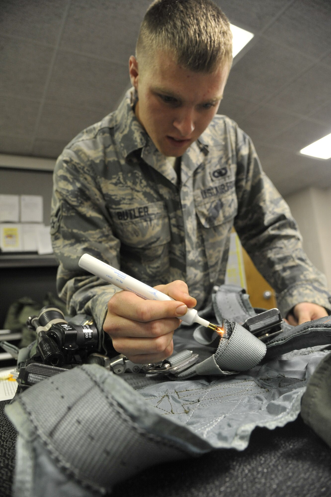 U.S. Air Force Airman 1st Class William Butler, 509th Operations Support Squadron aircrew flight equipment technician, sears frayed threads on a harness at Whiteman Air Force Base, Mo., Oct. 9, 2013. This process ensures the equipment is clean and free of any wear and tear. (U.S. Air Force photo by Airman 1st Class Keenan Berry/Released)